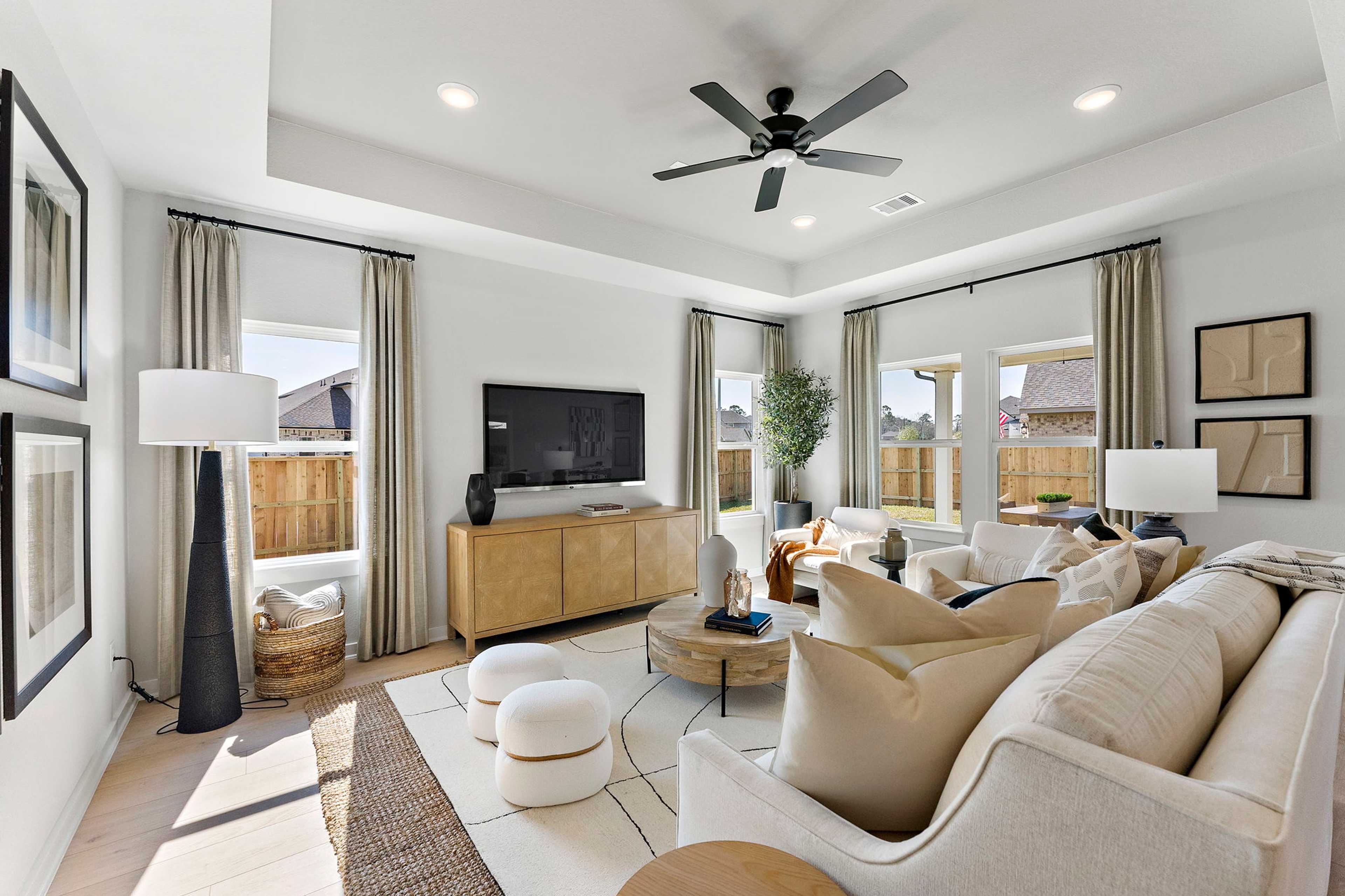 Spacious living room at Sundance Cove in Crosby TX with beige sectional sofa, ceiling fan, large windows, and wooden media console