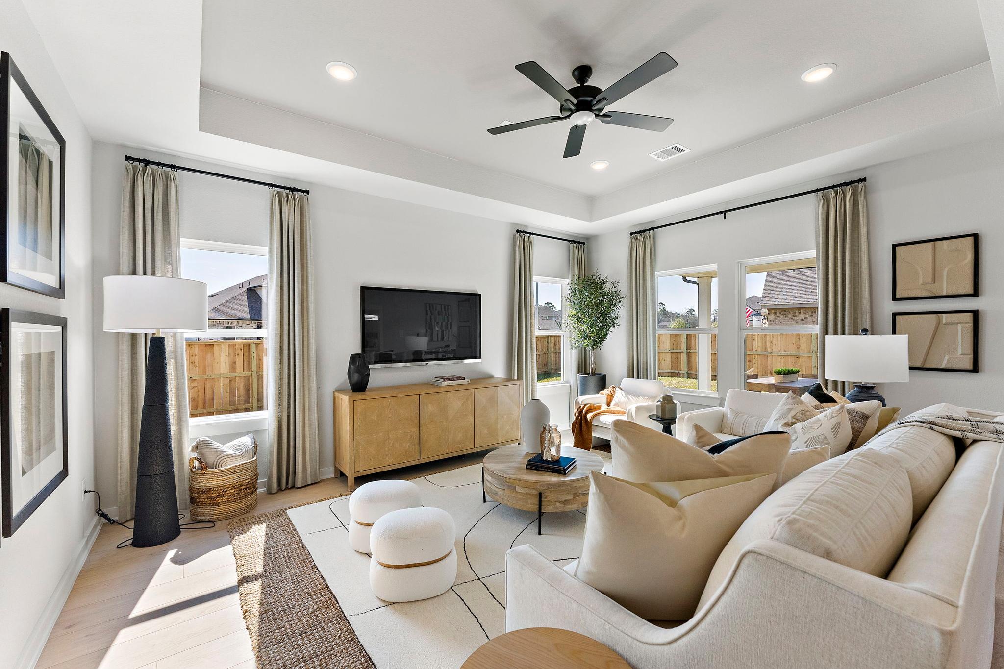 Spacious living room in Sundance Cove Crosby Texas with cream sectional sofa wooden media console ceiling fan and backyard views