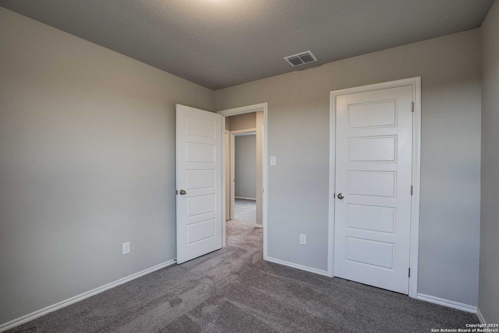 Neutral-toned secondary bedroom with paneled doors, carpet flooring, and hallway access in Davidson Homes The Blanco C, San Antonio