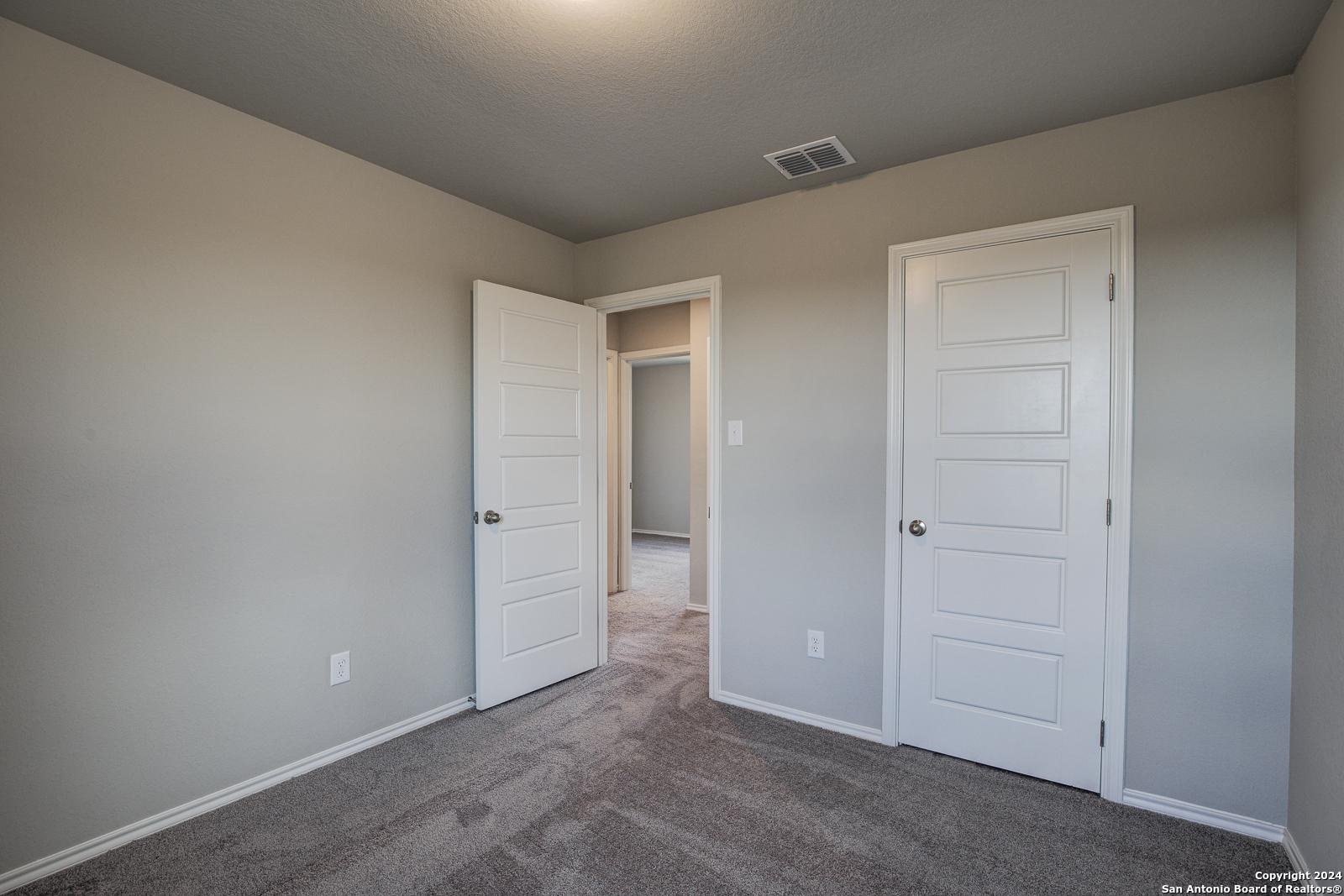 Cozy bedroom corner with beige walls, gray carpet, white panel doors, and open hallway in Davidson Homes The Blanco C, San Antonio, Texas