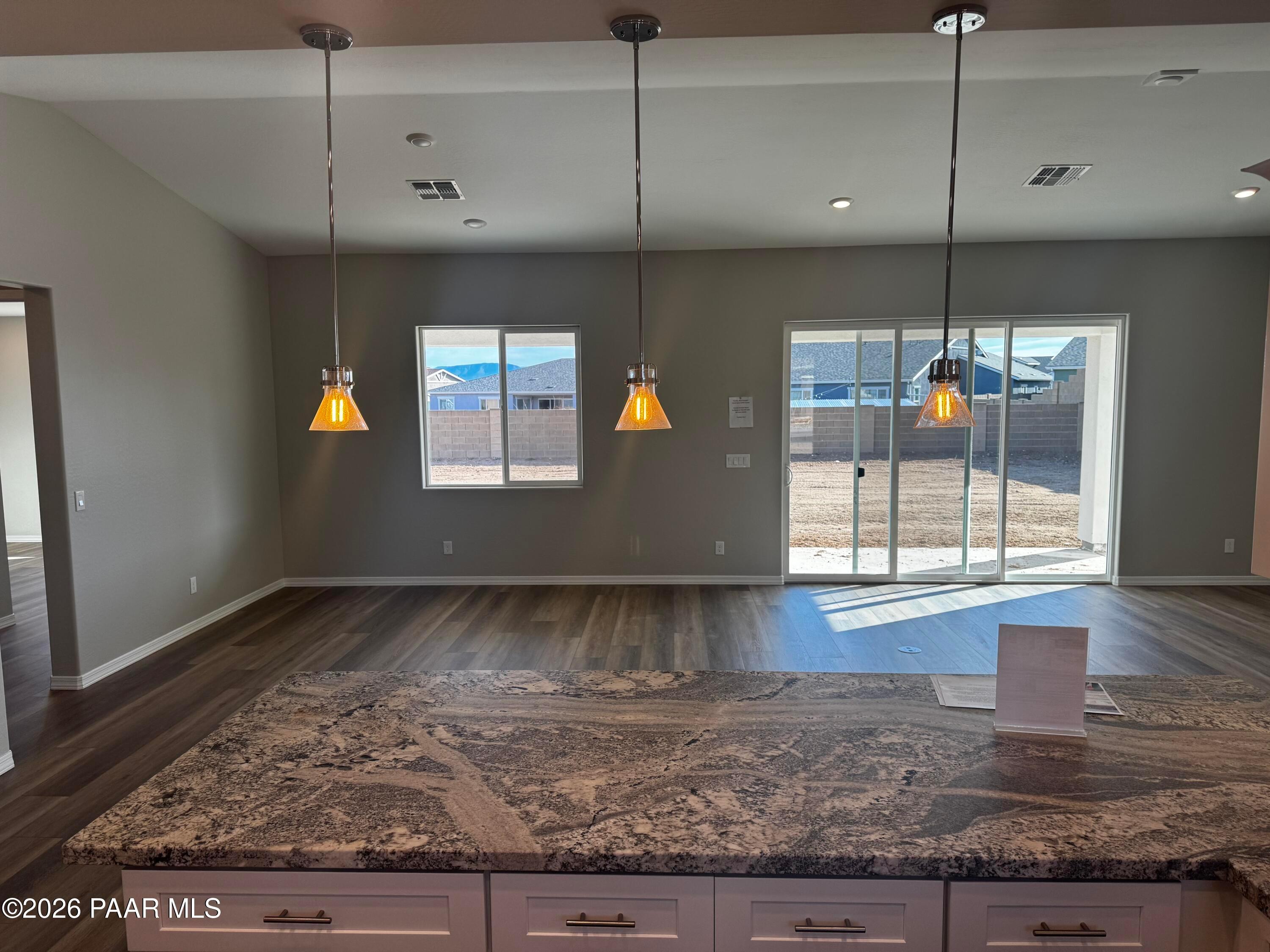 Modern open-concept kitchen with granite island, pendant lights, and sliding doors to backyard in Daybreak B, Prescott, AZ