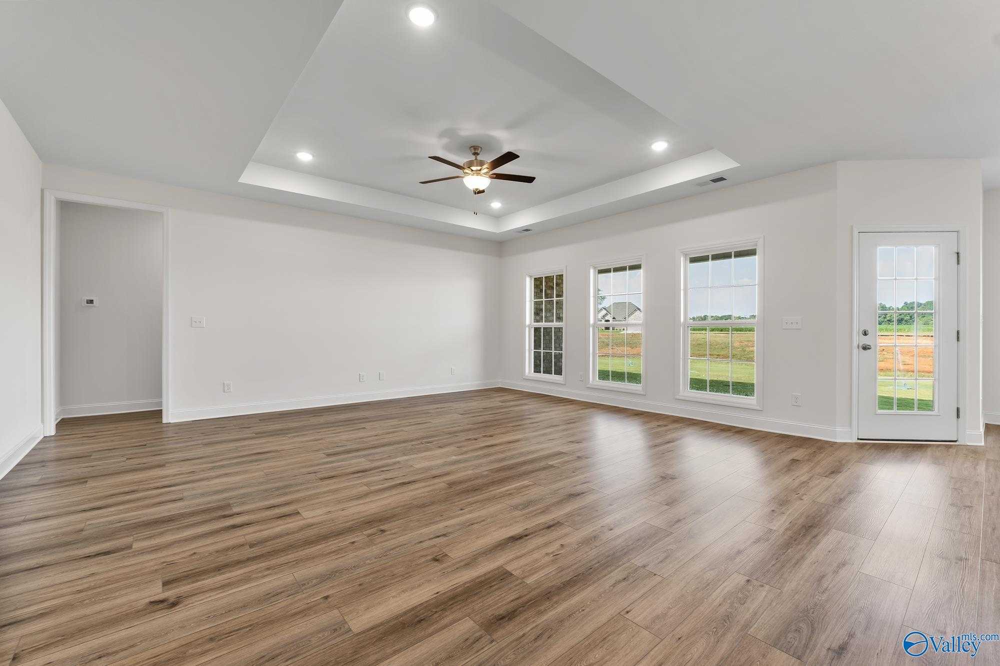 Bright living room with hardwood floors, ceiling fan, and large windows overlooking fields in Davidson Homes The Harrison, Meridianville