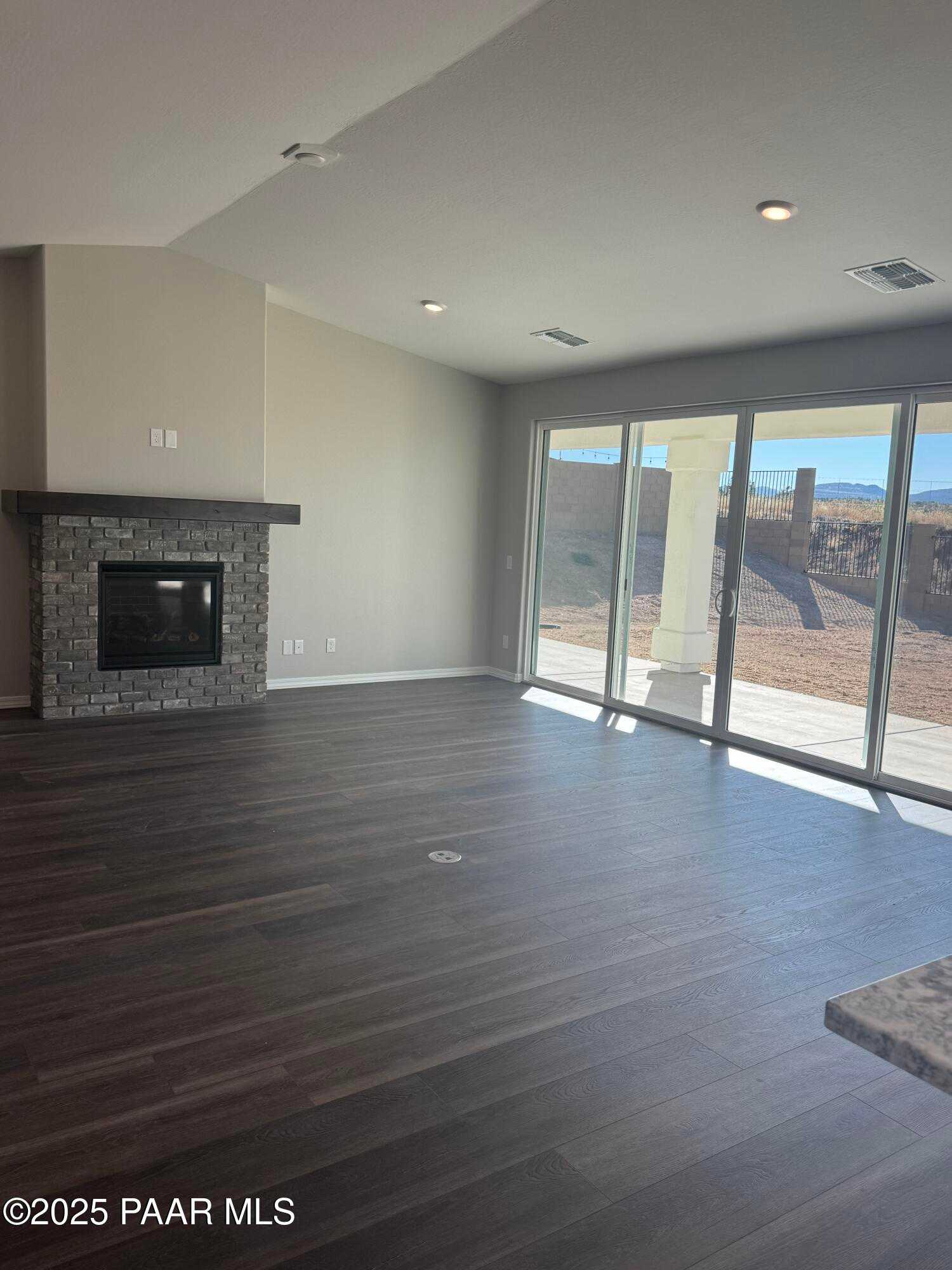 Spacious living room with stone gas fireplace, sliding doors to desert patio, and mountain views in Davidson Homes The Monarch E, Prescott Arizona