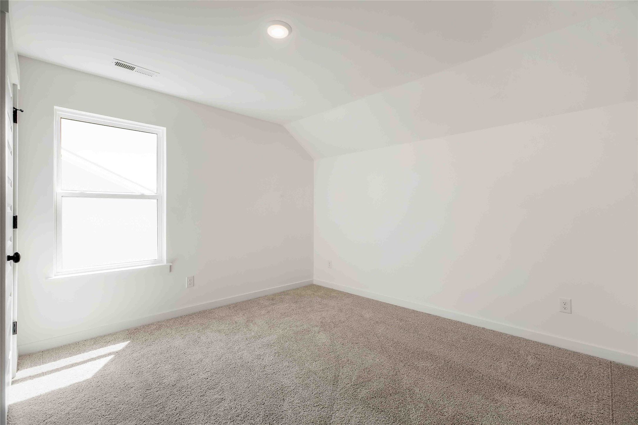 Bright, carpeted bedroom with vaulted ceilings in The Ash O floor plan by Davidson Homes in Heartland, Texas.