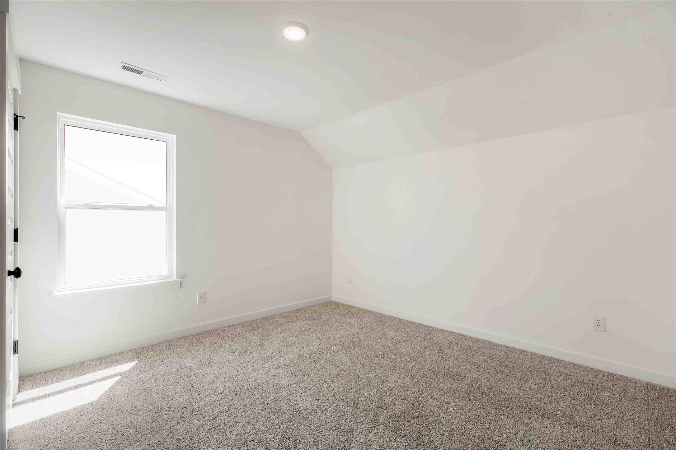 Bright, carpeted bedroom with vaulted ceilings in The Ash O floor plan by Davidson Homes in Heartland, Texas.