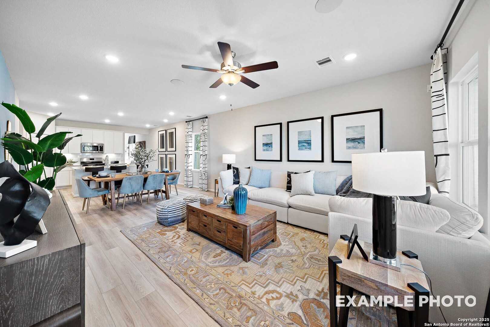 Open-concept living and dining area with white sofa, wooden table, ceiling fans, and kitchen view in Davidson Homes San Marcos D, San Antonio