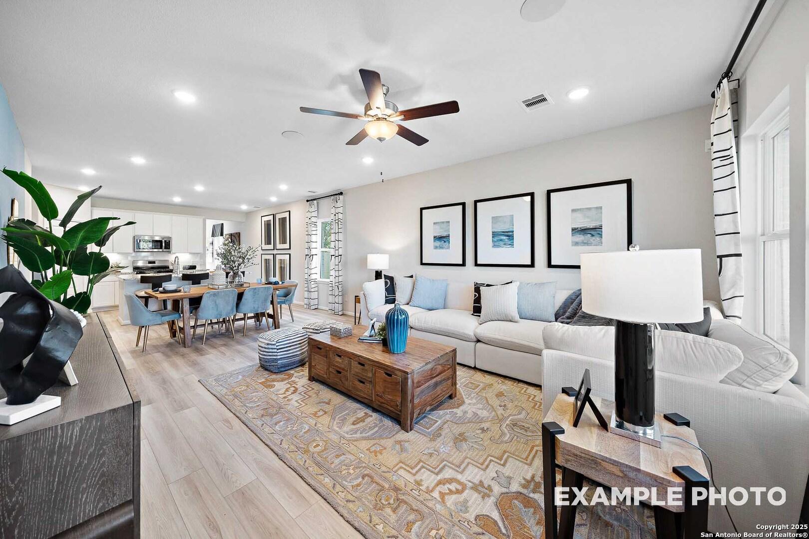 Open-concept living and dining area with white sofa, wooden table, ceiling fans, and kitchen view in Davidson Homes San Marcos D, San Antonio