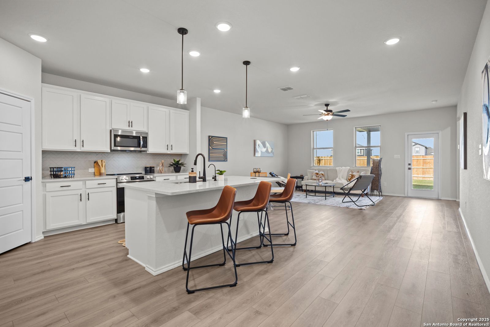 Open-concept kitchen-living area with white island, orange bar stools, hardwood floors, and backyard view in Davidson Homes The Douglas C, Seguin, Texas