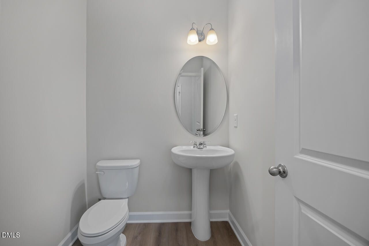 Bright powder room with pedestal sink, round mirror, and white toilet in The Gavin B, Davidson Homes, Lillington, NC