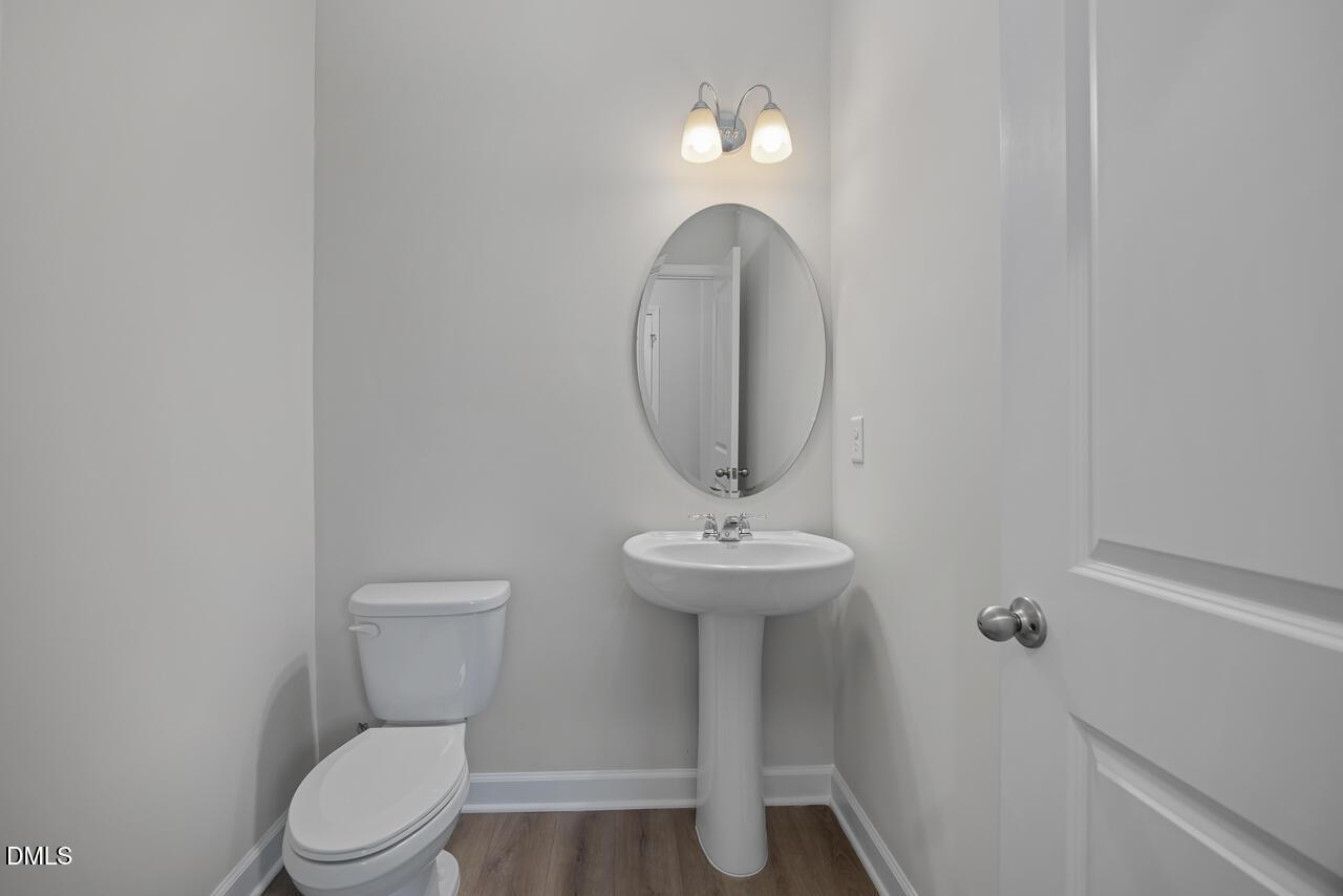Bright powder room with pedestal sink, round mirror, and white toilet in The Gavin B, Davidson Homes, Lillington, NC