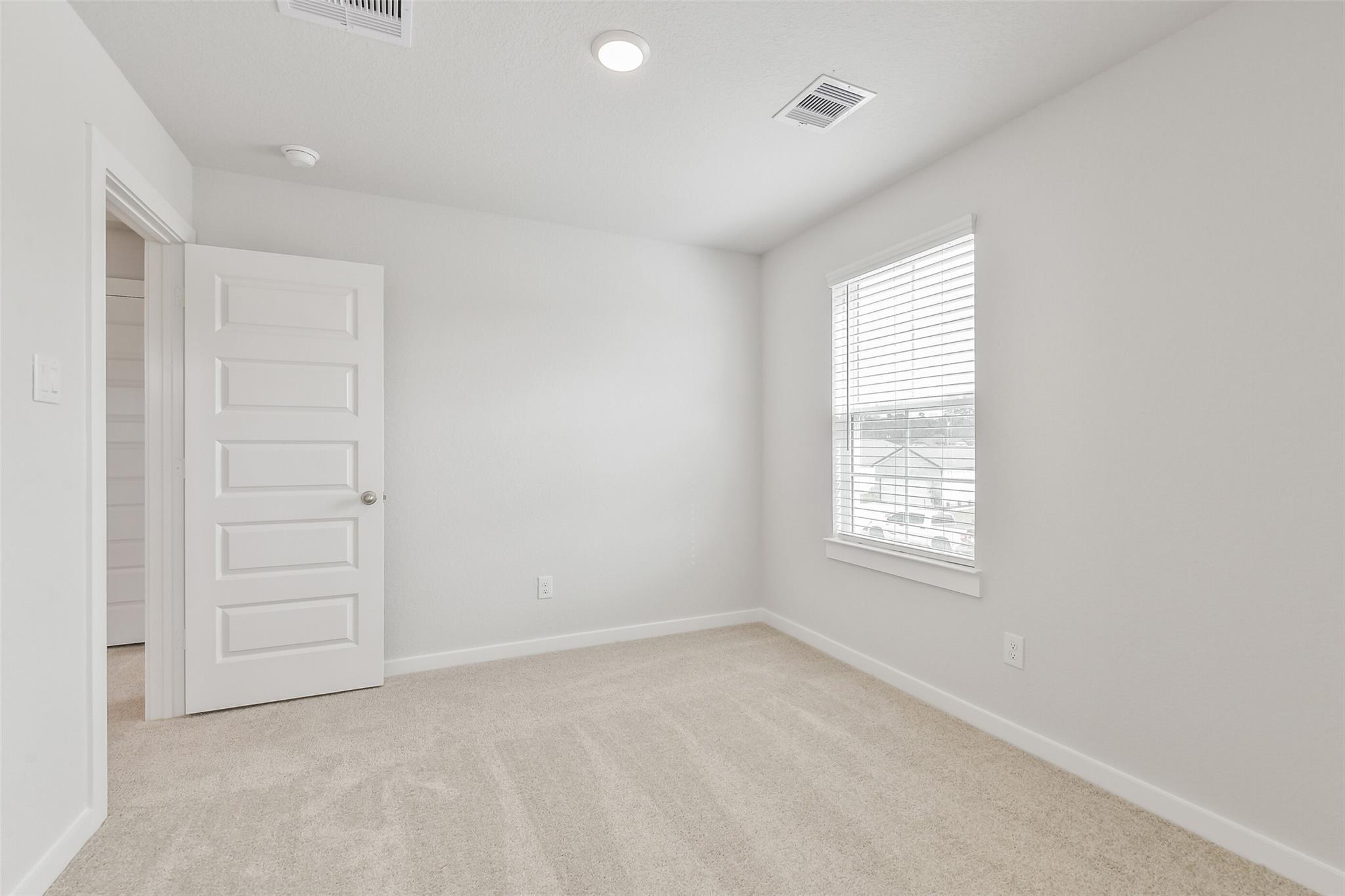 Bright secondary bedroom with beige carpet, white door, and window blinds in Davidson Homes The Brazos E, Cleveland TX