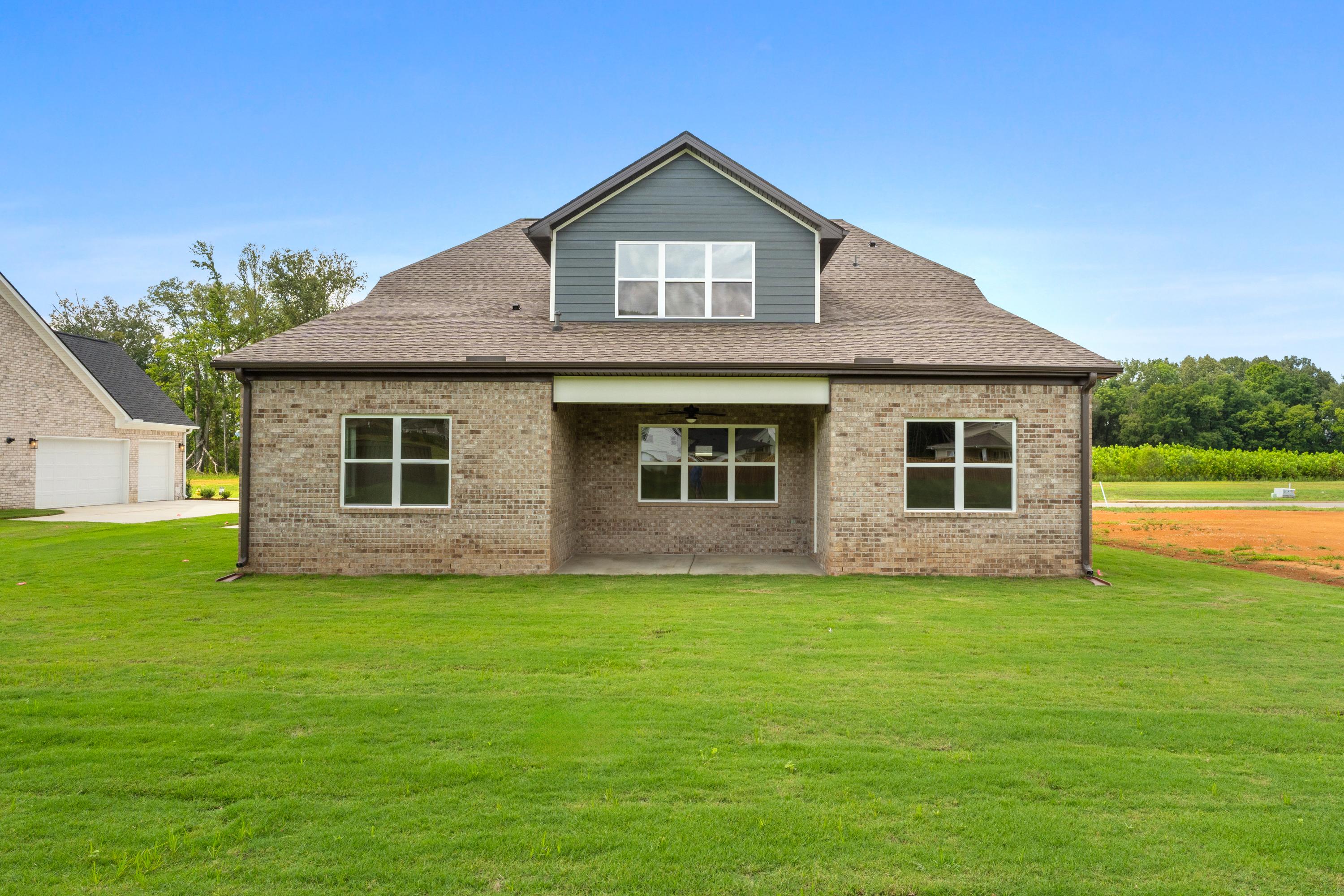 Two-story brick facade of The Oxford C home featuring covered entry porch, gabled dormer, and 3-car garage on lush green lawn