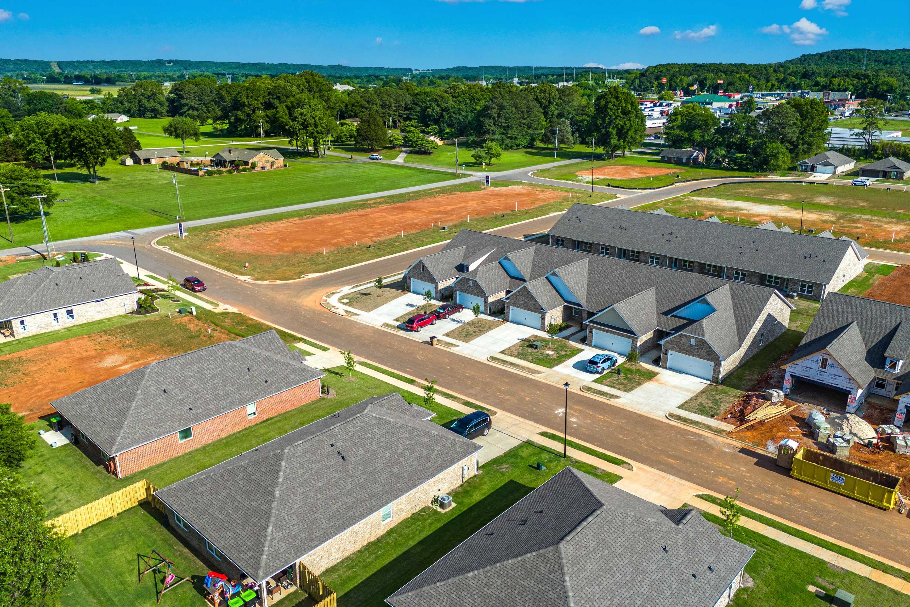 Aerial view of new homes under construction at The Retreat at Hollon Meadow in Decatur, Alabama with gray roofs, green lawns and wooded backdrop