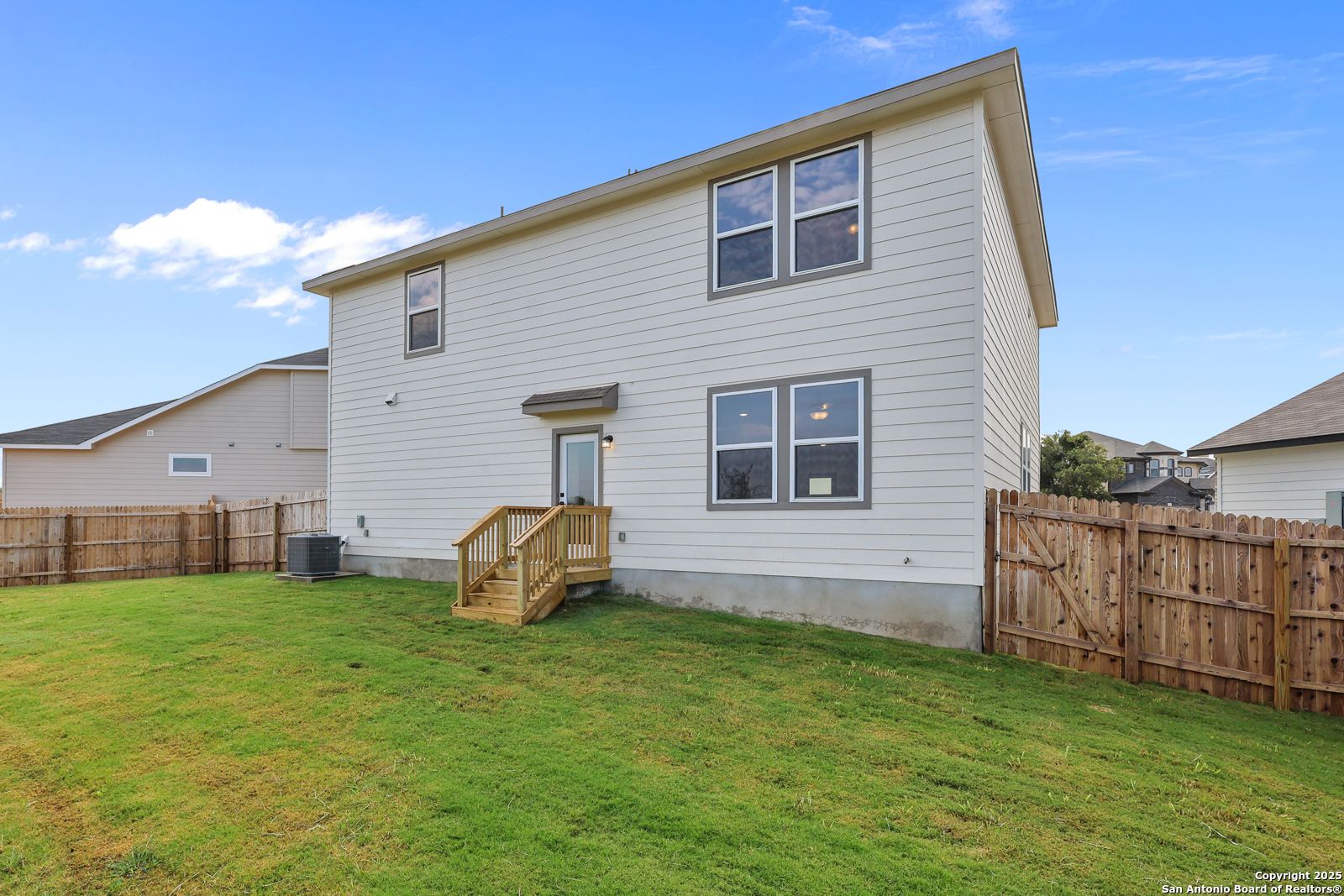 Two-story beige home with wooden deck stairs, glass back door, and fenced grassy yard in Royal Crest, San Antonio, Texas