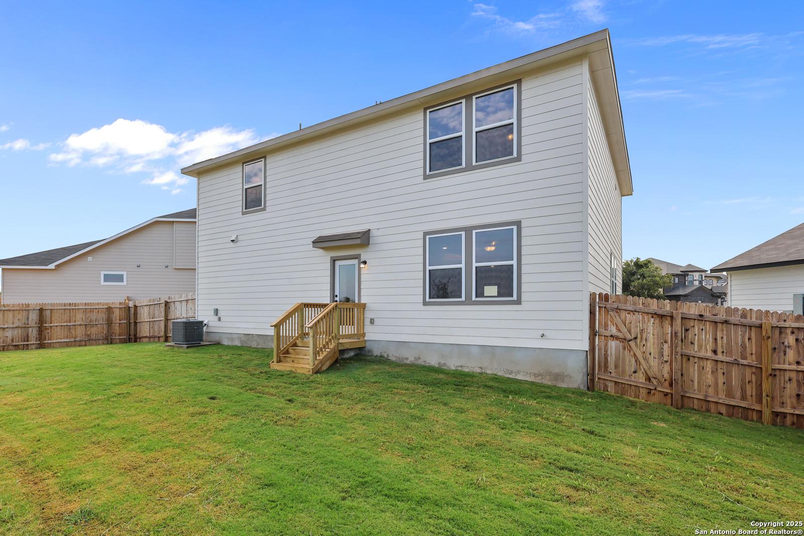 Two-story beige home with wooden deck stairs, glass back door, and fenced grassy yard in Royal Crest, San Antonio, Texas