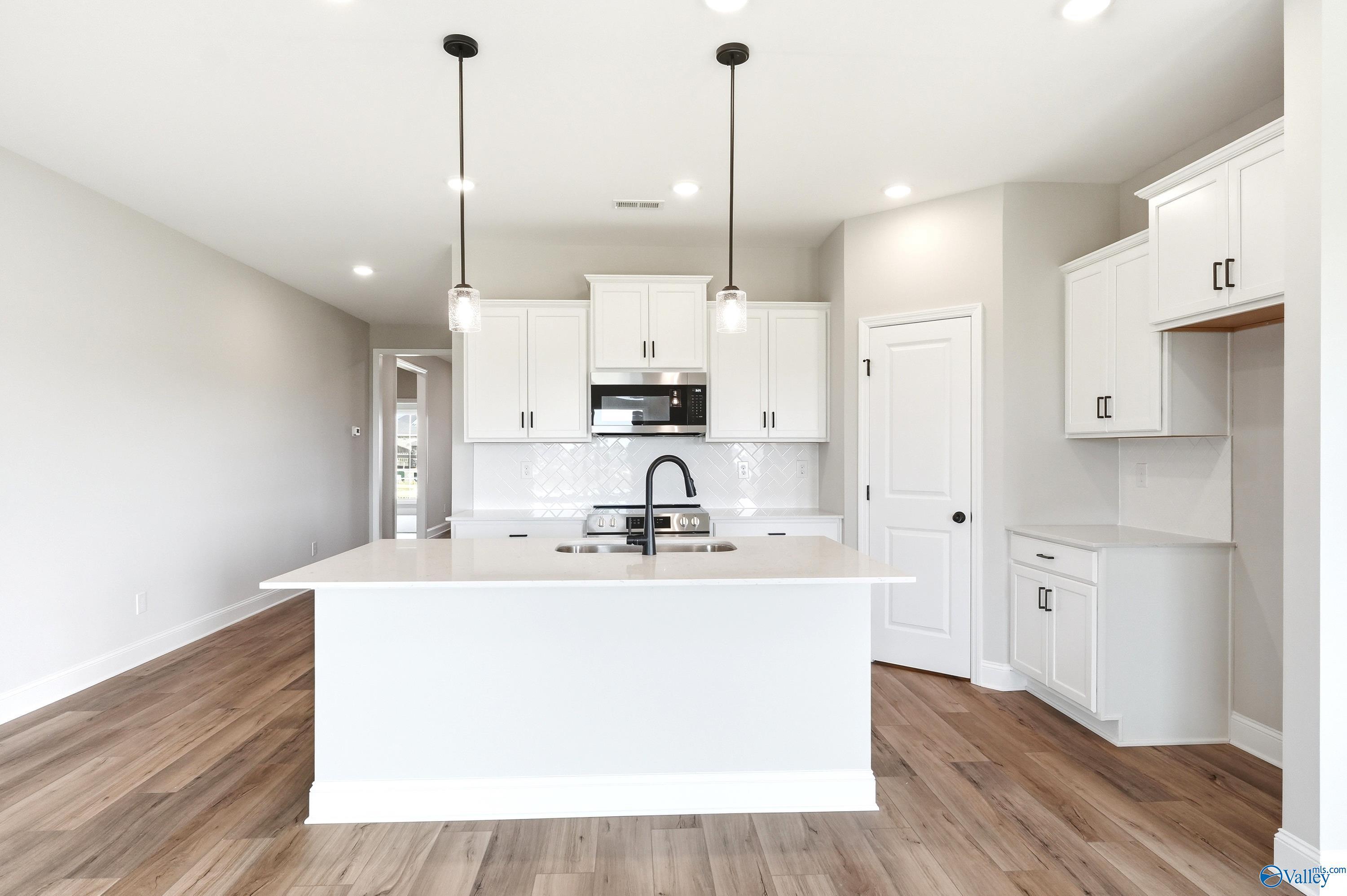 Modern kitchen with white cabinets, island, and wood floors in The Daphne D plan at Creekside in Harvest, Alabama.