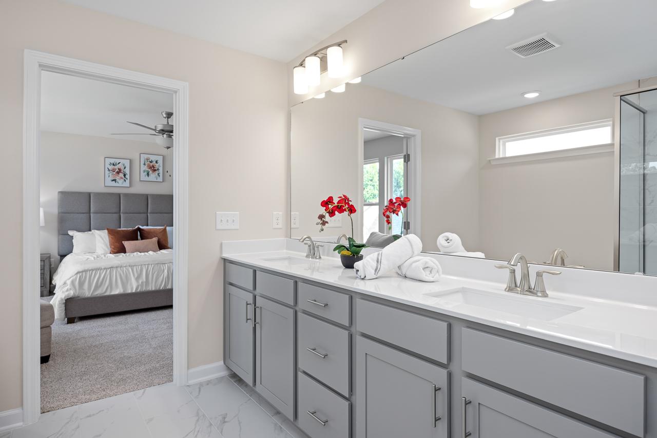 Spacious master bathroom in The Chestnut featuring a dual-sink vanity with grey cabinets and views into the master suite.