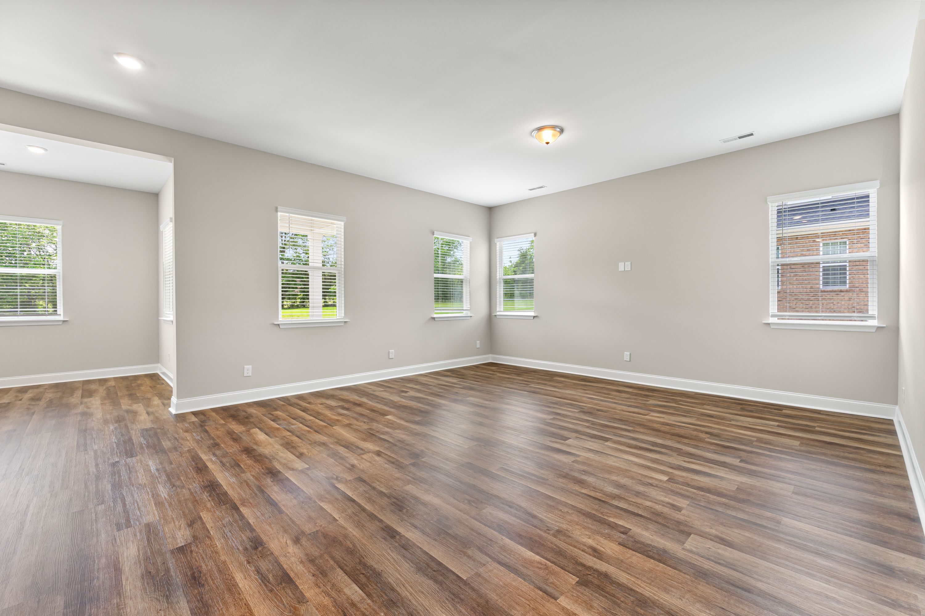 Spacious master bedroom in The Arcadia E showcasing hardwood floors, gray walls, large windows, and open layout