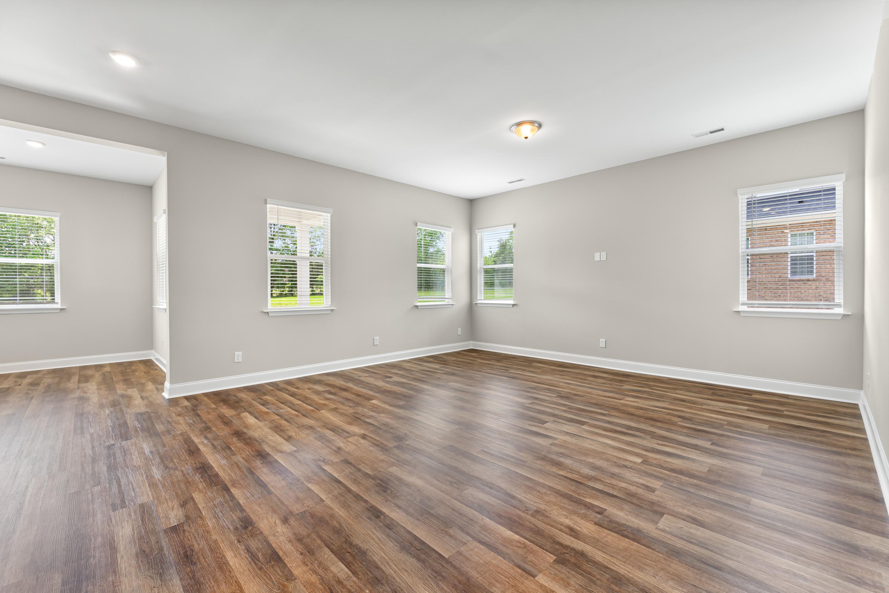 Spacious master bedroom in The Arcadia B with light gray walls, large windows, and hardwood floors