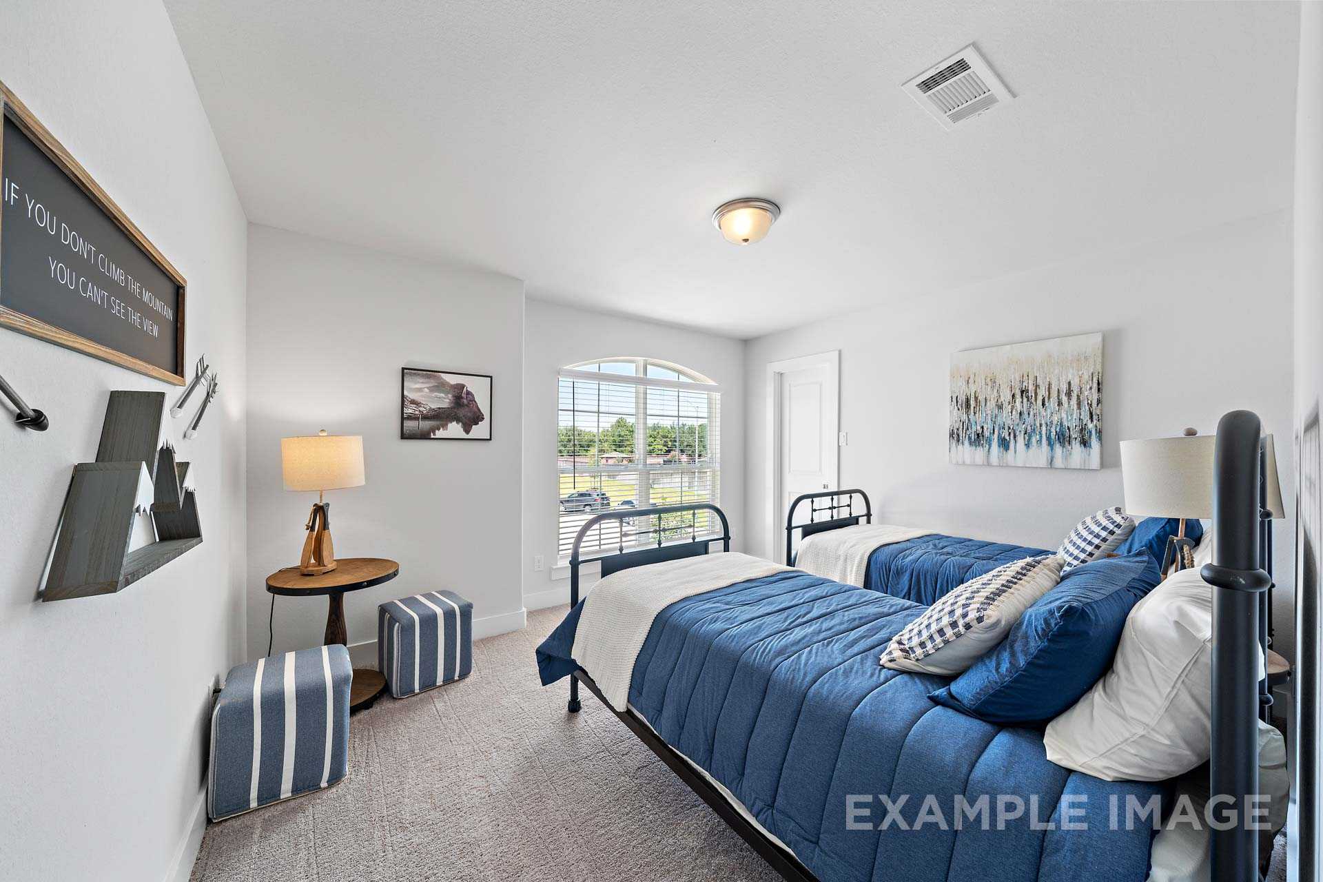 Cozy twin bedroom in The Rose B with blue bedding, white walls, large window, and inspirational wall art
