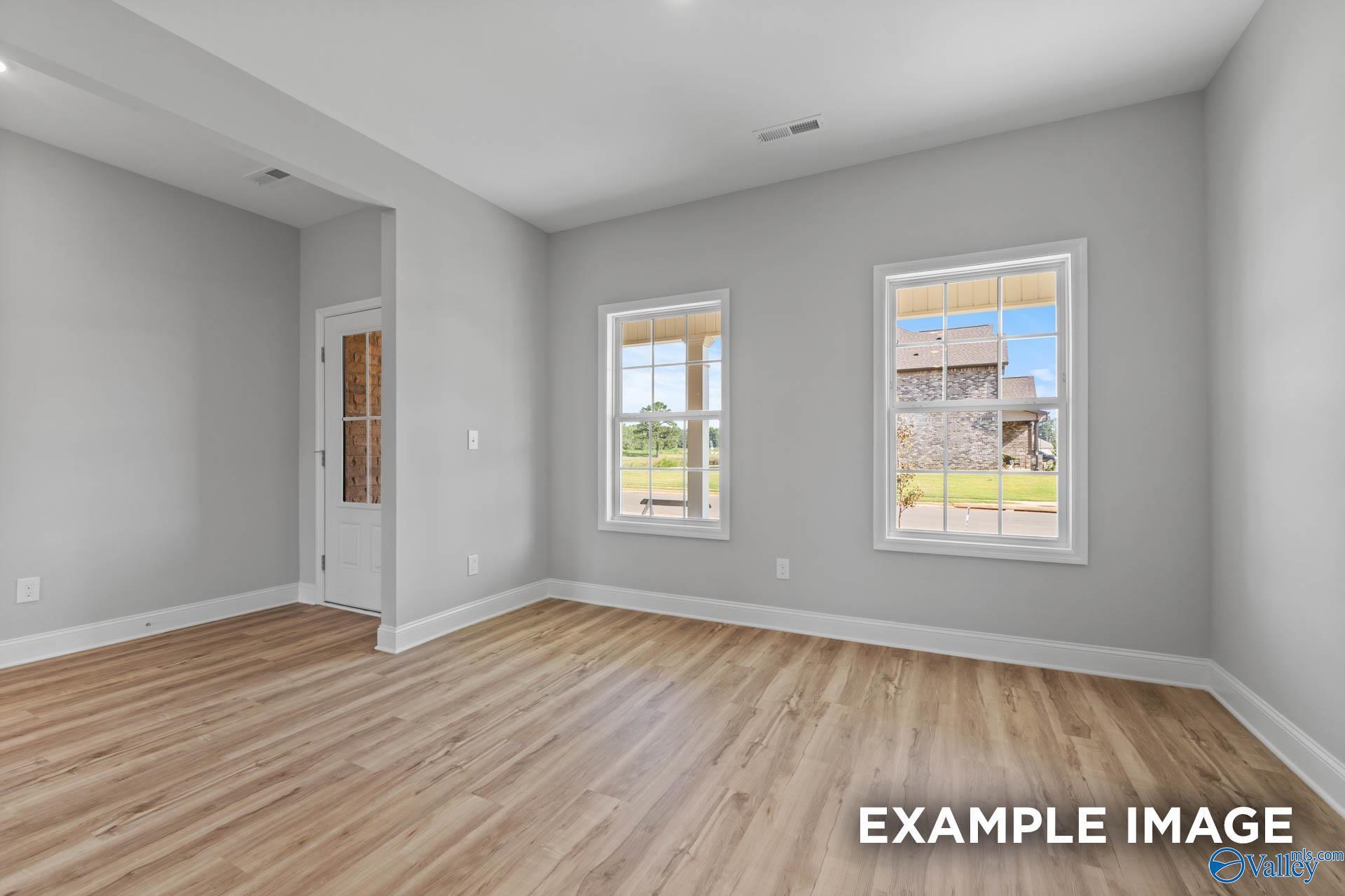 Bright living room with light gray walls, hardwood floors, and large windows overlooking green yard in Davidson Homes The Shelby B, New Market, Alabama