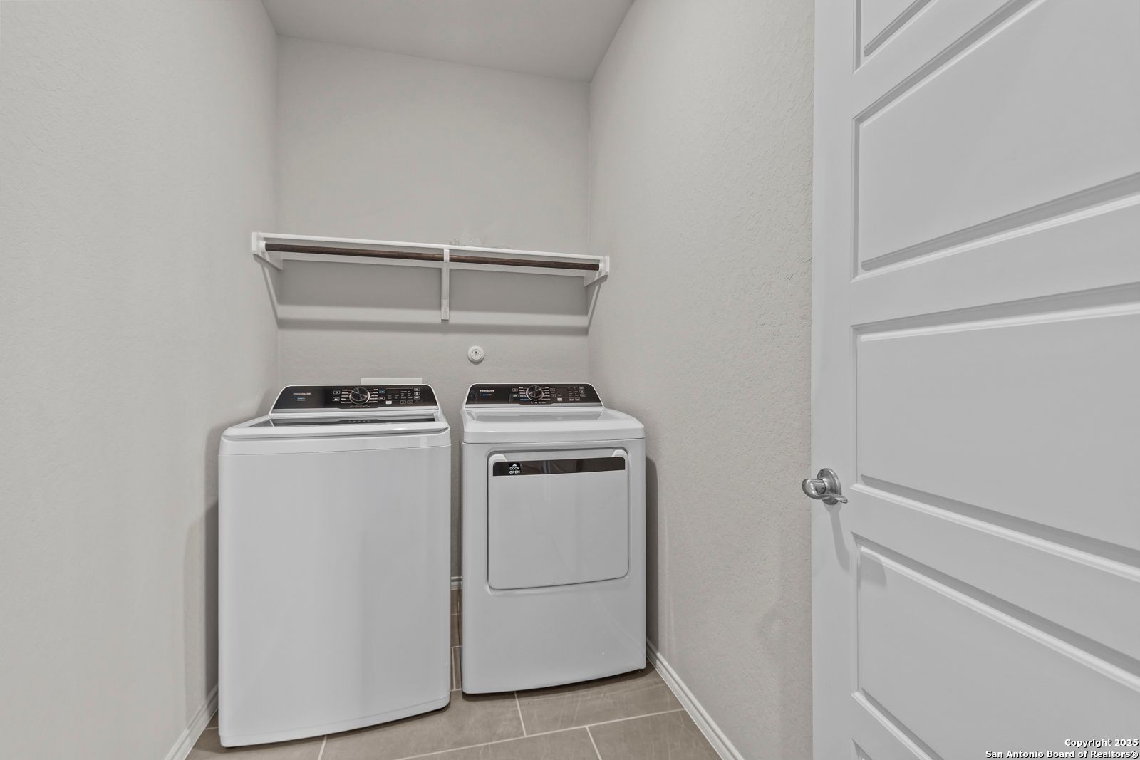 Functional laundry room with white front-load washer dryer and open shelving in Davidson Homes The Collin B, Seguin, Texas