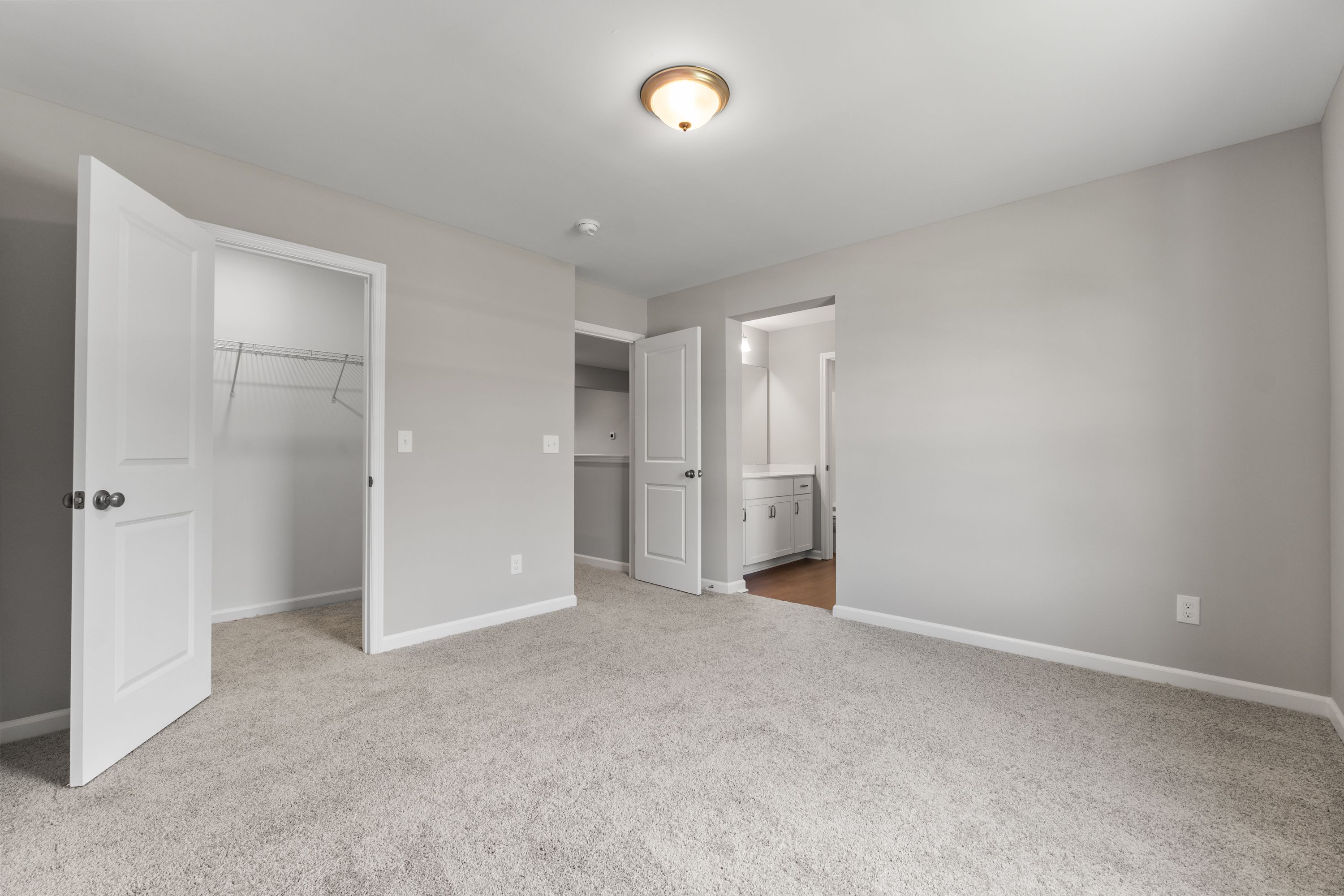 Spacious master bedroom in The Avalon E featuring open walk-in closet, en-suite bathroom, gray walls, and carpet flooring