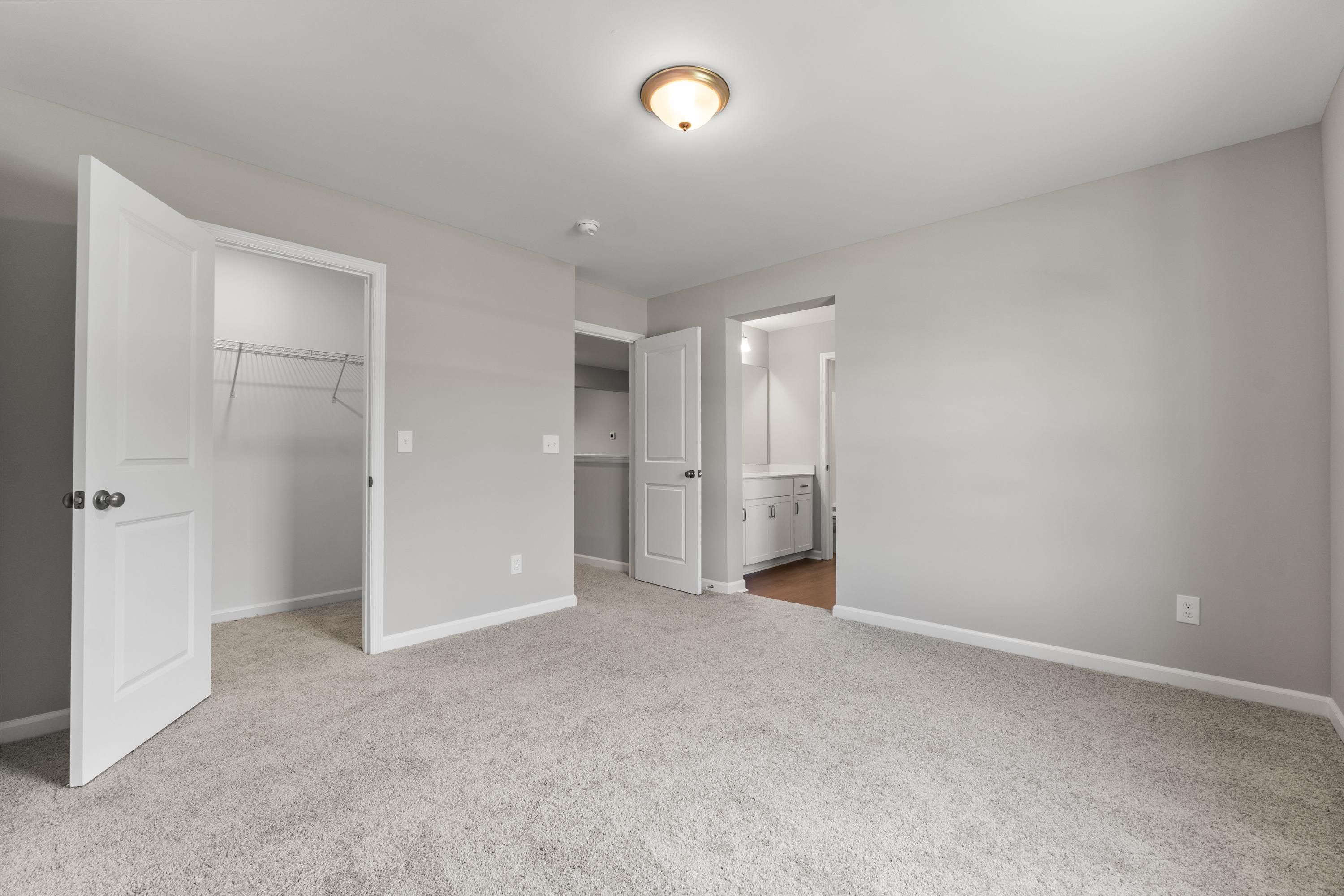 Spacious master bedroom in The Avalon D with open walk-in closet, en-suite bath, gray walls, carpet floor