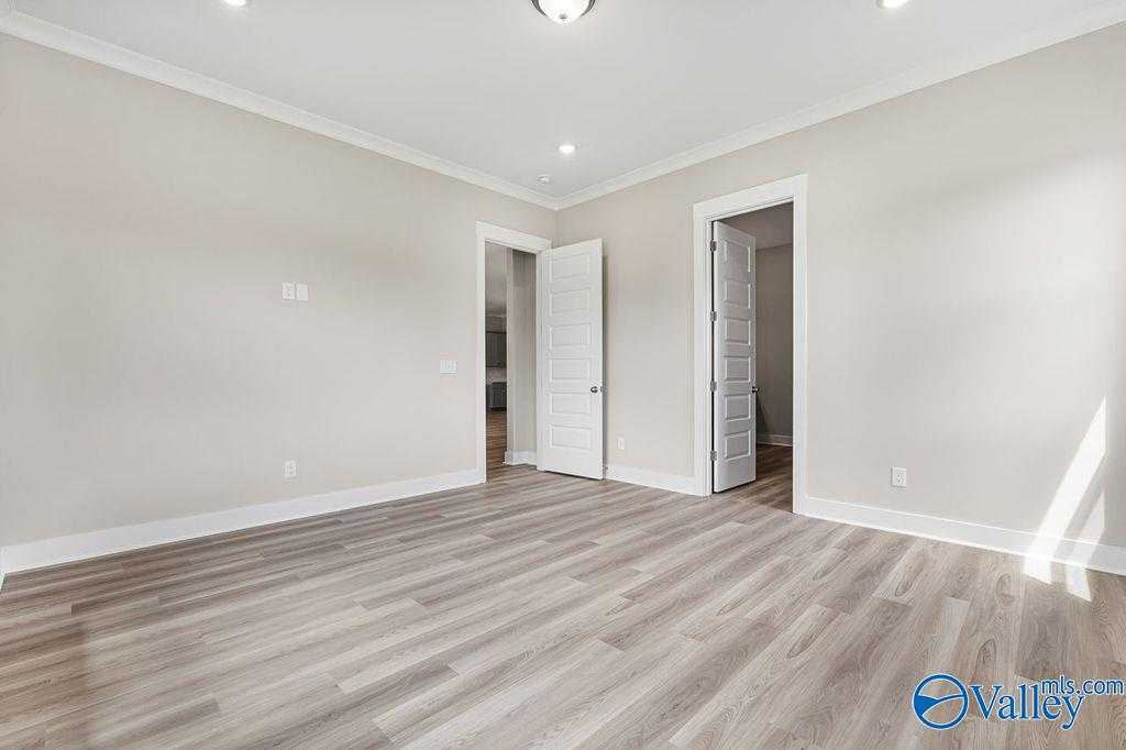 Empty bedroom with beige walls, light oak floors, ceiling fan, and adjacent doorways in Evermore Homes The Oxford, Owens Cross Roads, AL