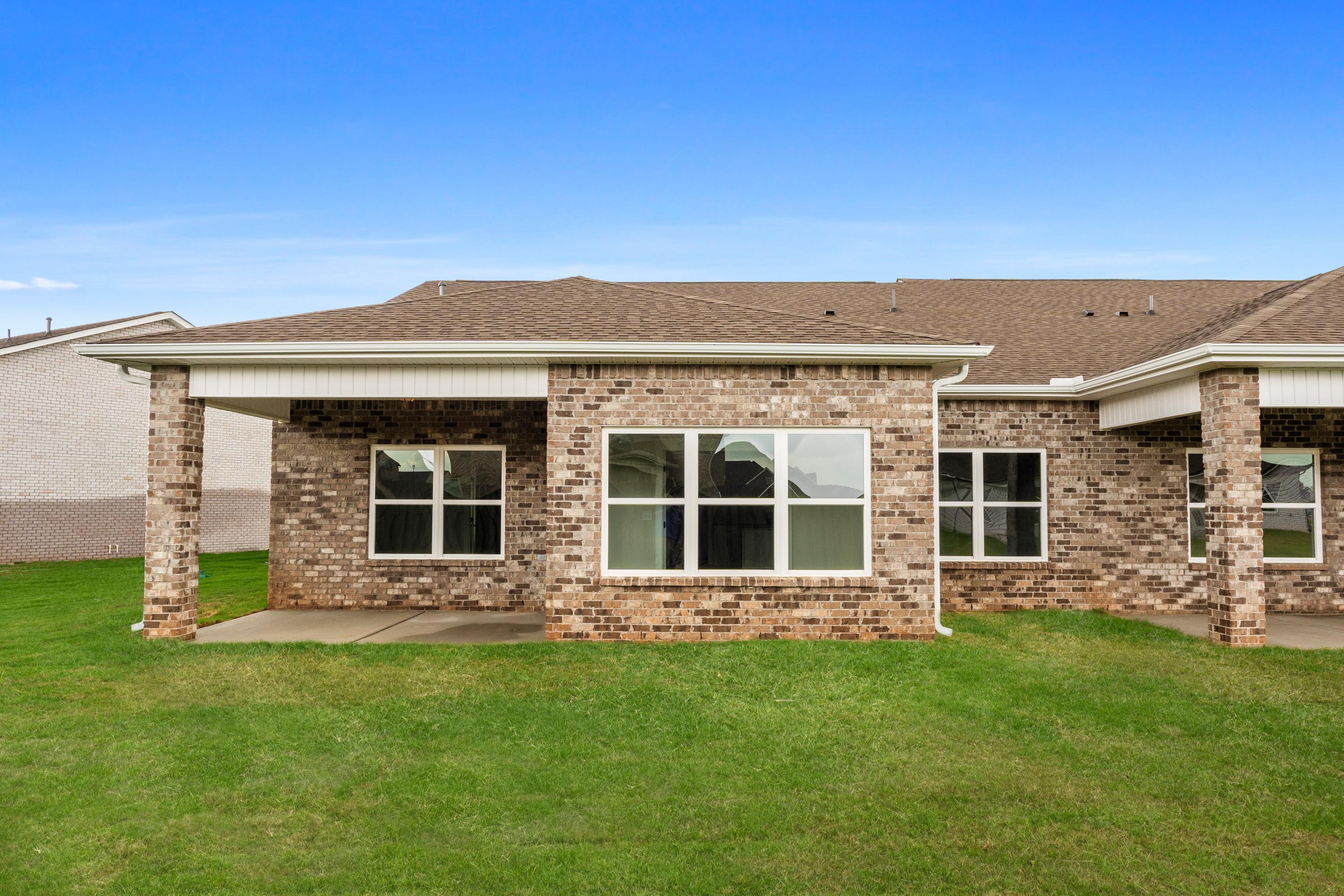 Brick home exterior with covered patio at The Villas at Barnett's Crossing in Madison, Alabama featuring large windows and green lawn
