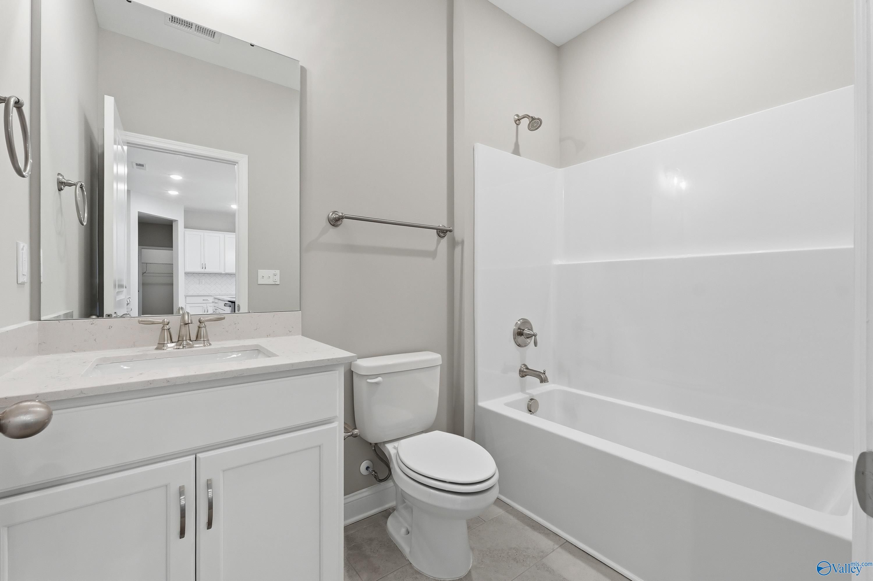 Spacious bathroom with white tub, glass shower, single vanity sink, and toilet in Davidson Homes The Lanier, Toney, Alabama