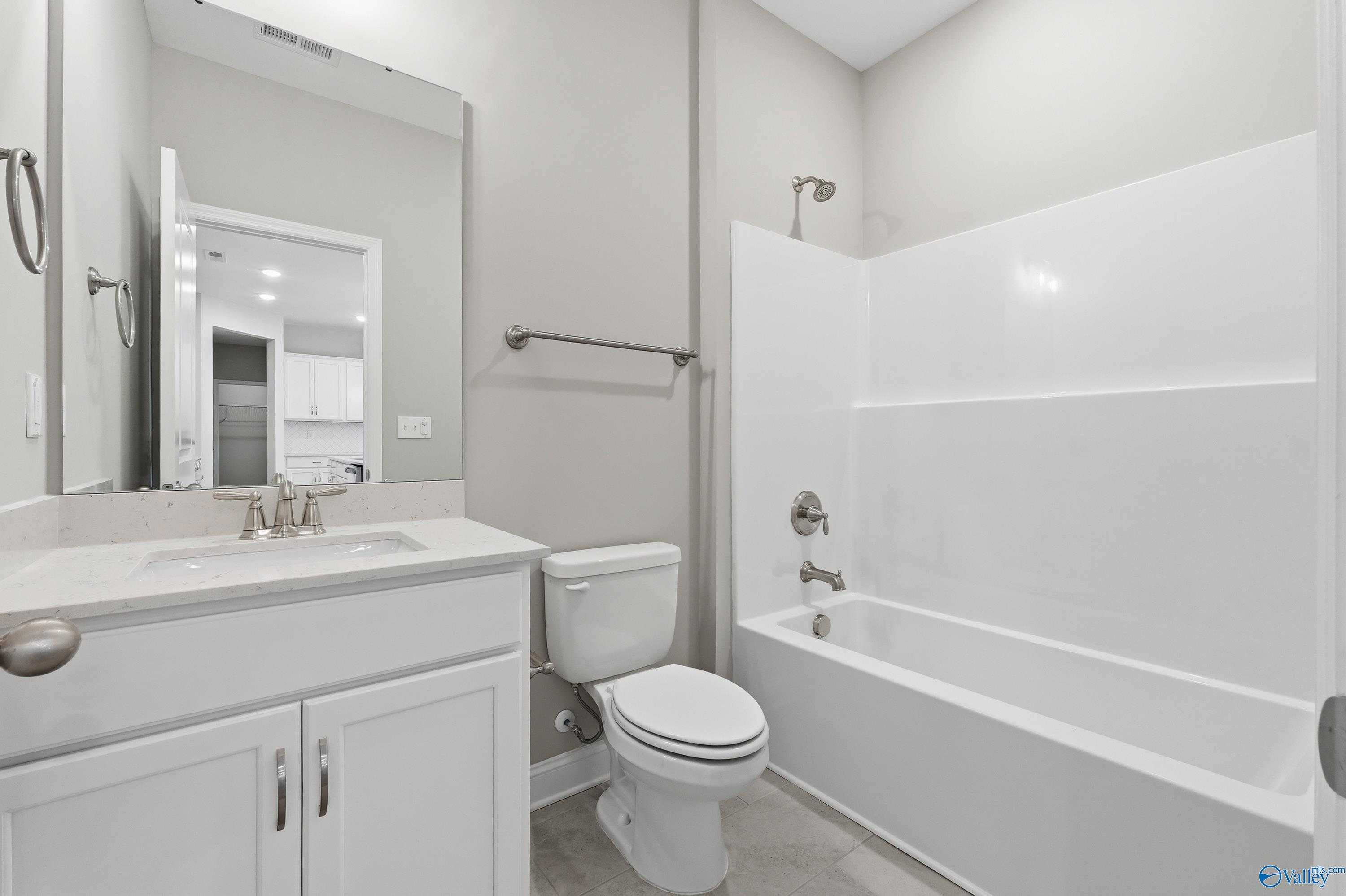 Spacious bathroom with white tub, glass shower, single vanity sink, and toilet in Davidson Homes The Lanier, Toney, Alabama
