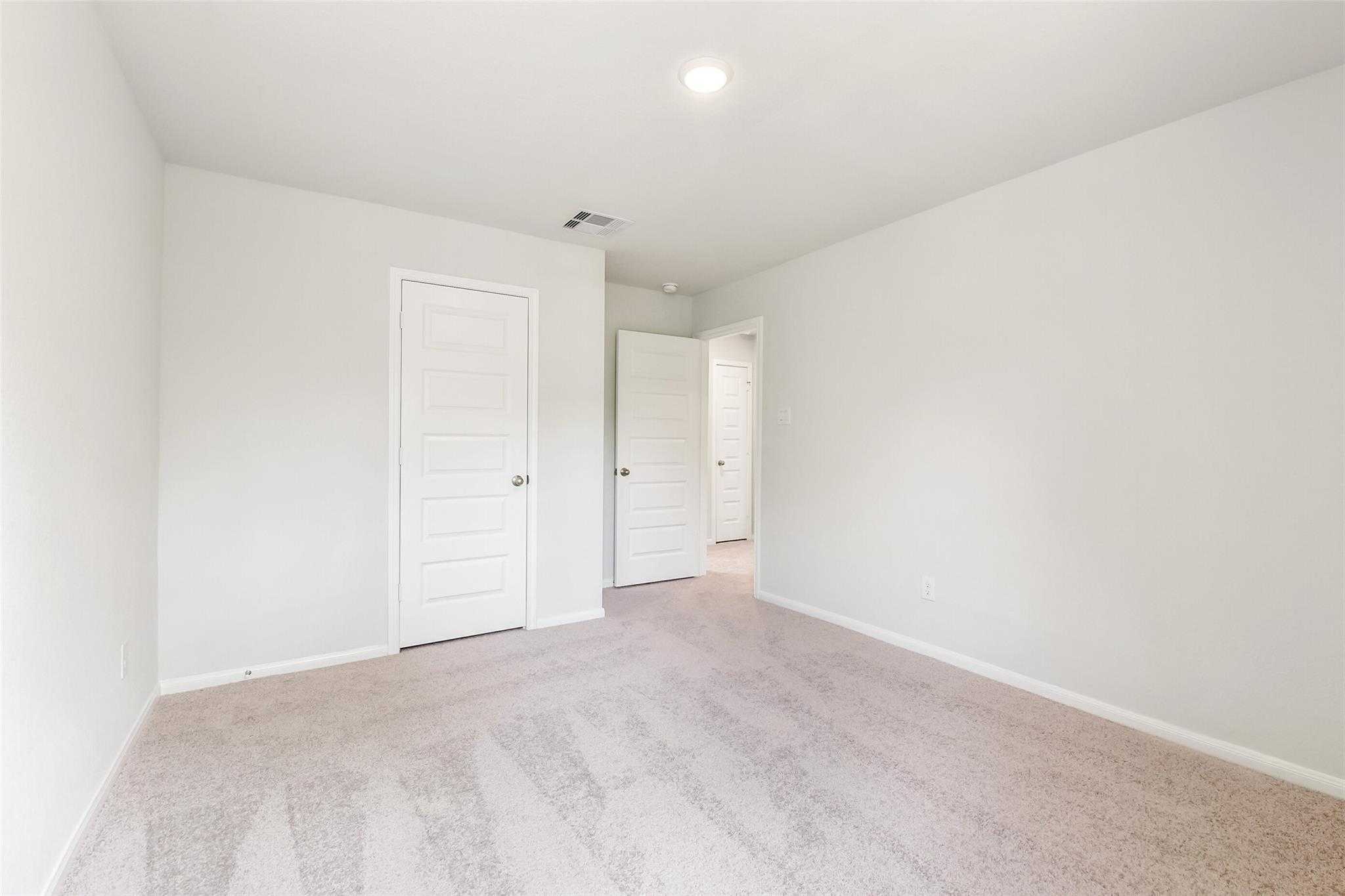 Spacious secondary bedroom with light gray walls, beige carpet, white paneled doors in Davidson Homes The Sabine E, Conroe, Texas