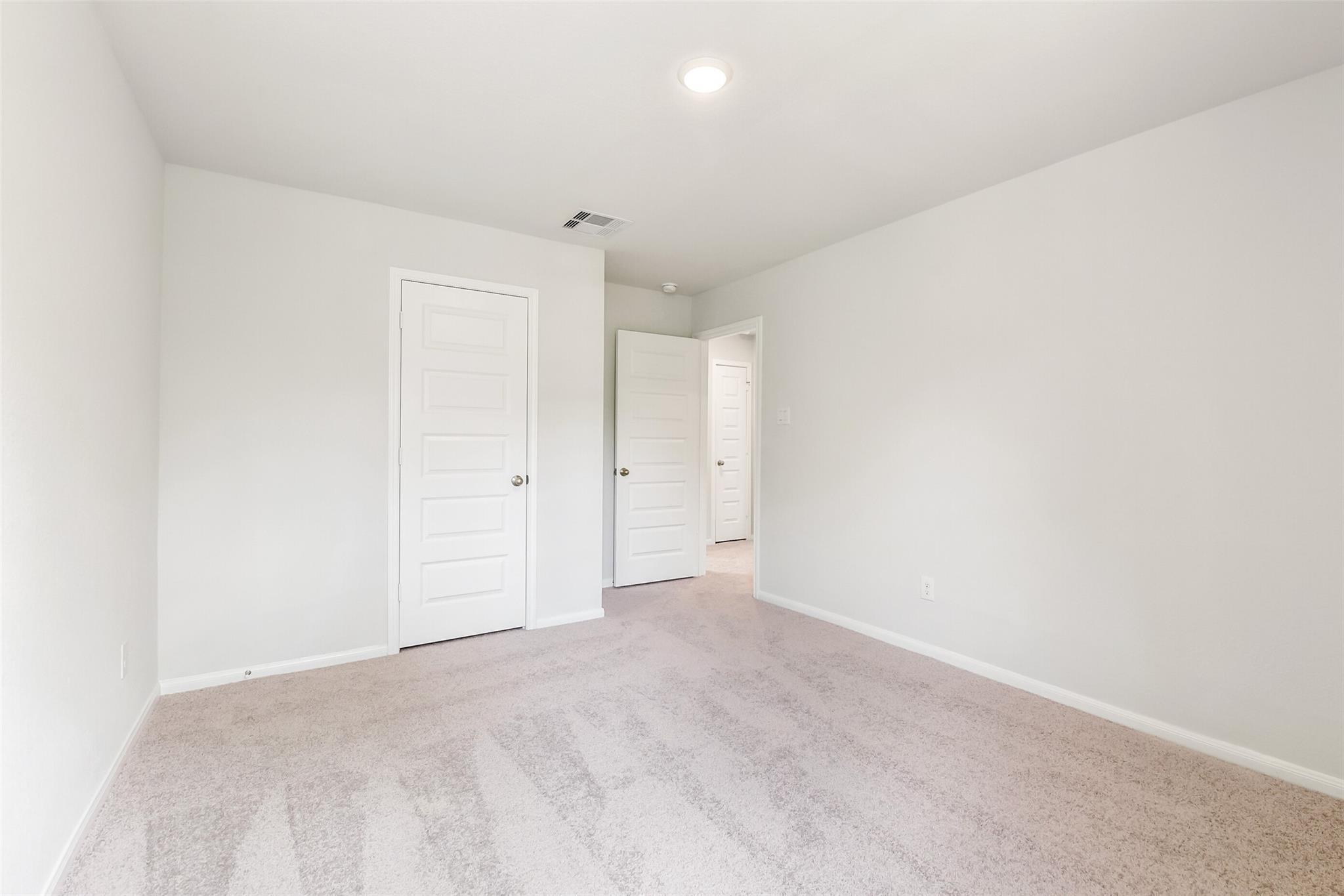 Spacious secondary bedroom with light gray walls, beige carpet, white paneled doors in Davidson Homes The Sabine E, Conroe, Texas