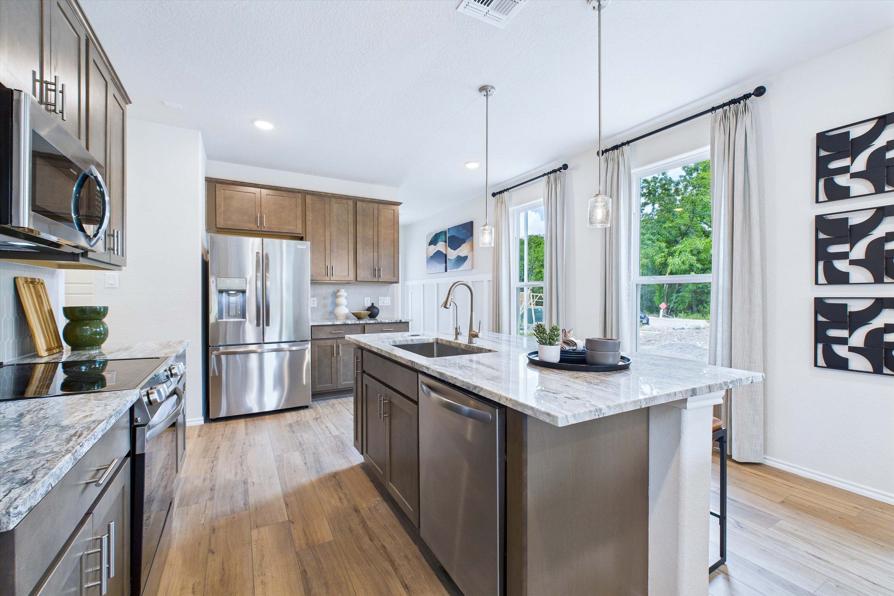 Modern kitchen in The Gillian C featuring a spacious granite island, stainless steel appliances, and wood-style flooring.