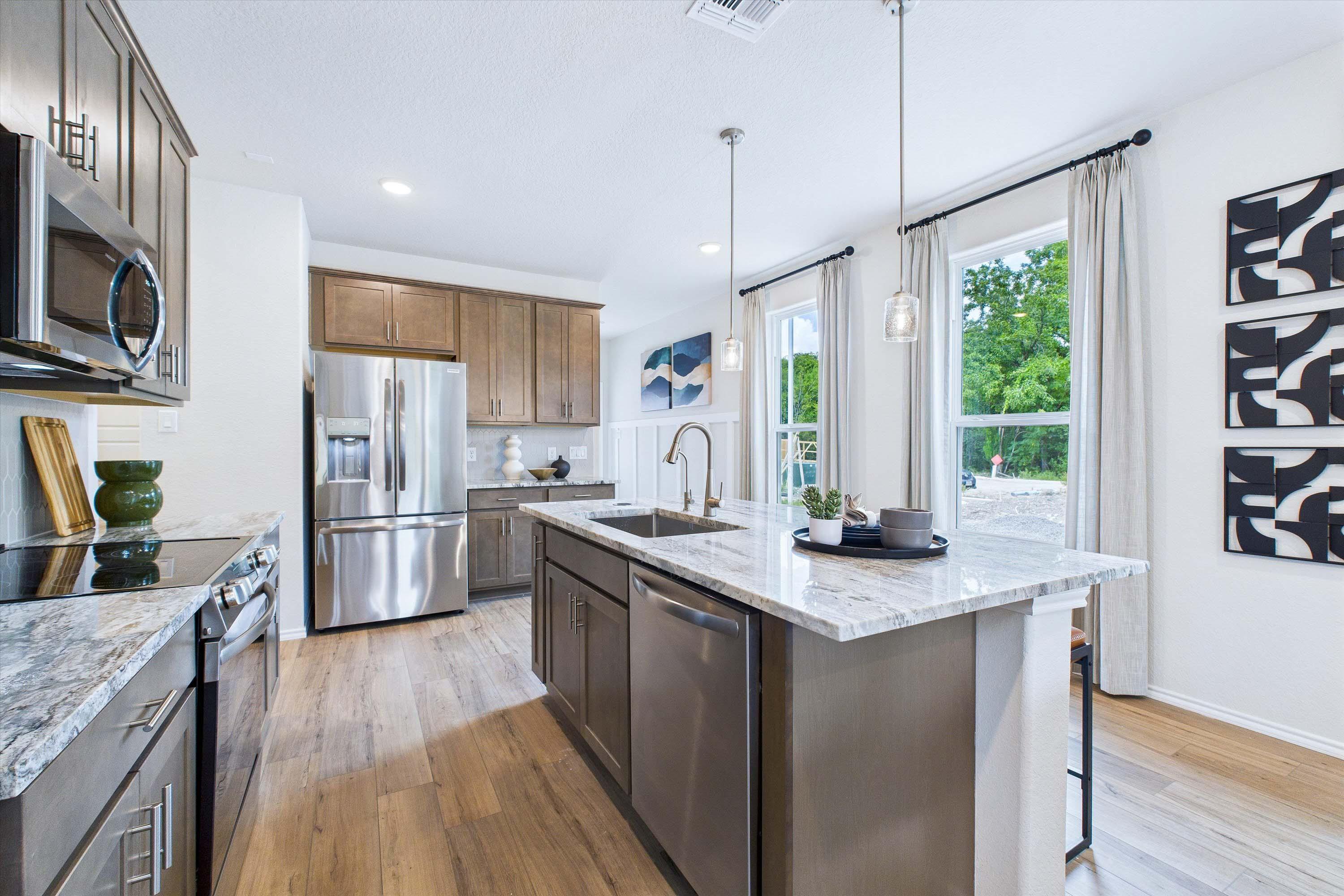 Modern kitchen in The Gillian C featuring a spacious granite island, stainless steel appliances, and wood-style flooring.