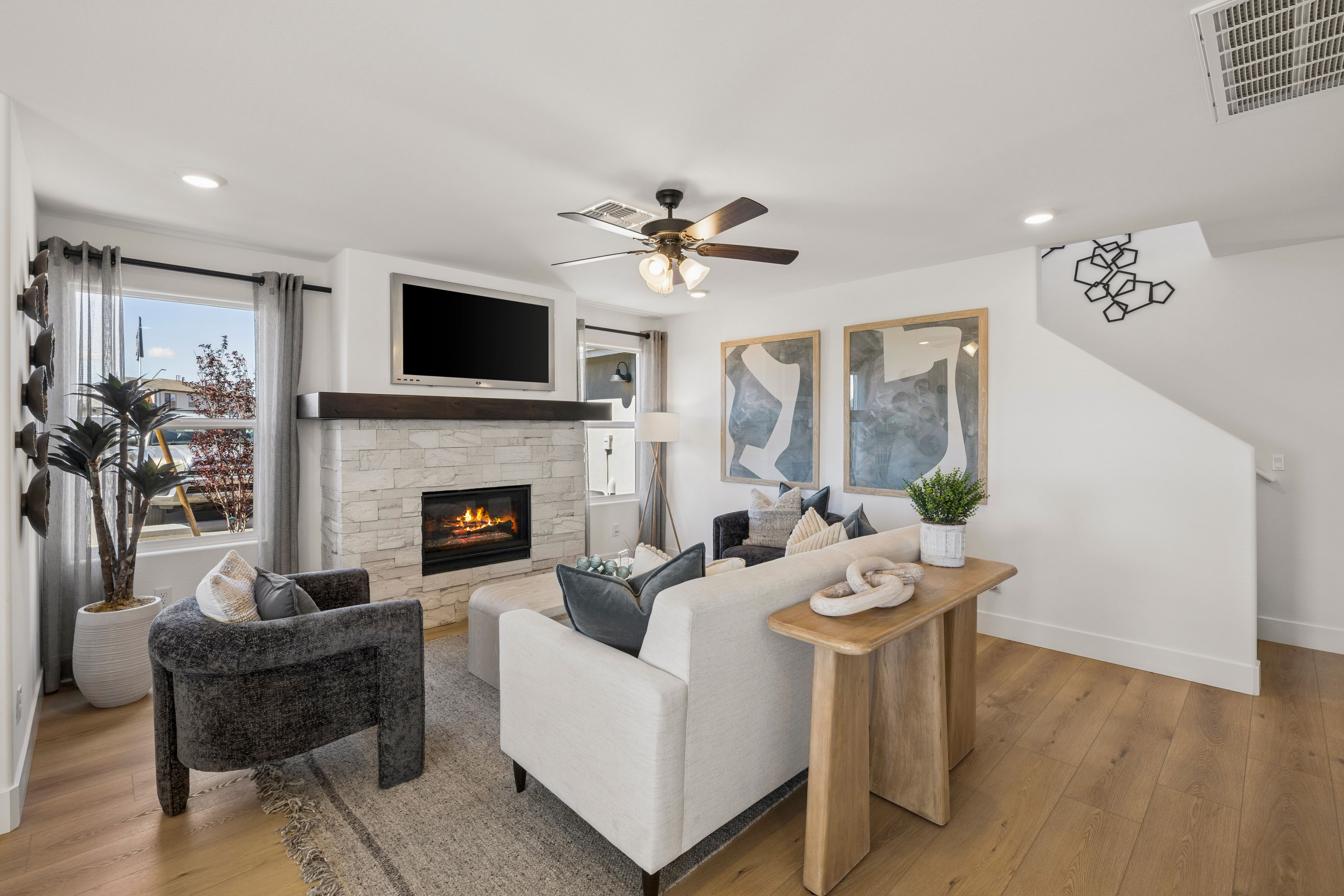 Cozy living room with stone gas fireplace, white sofa, gray armchair, hardwood floors at South Ranch Southern Collection in Prescott AZ