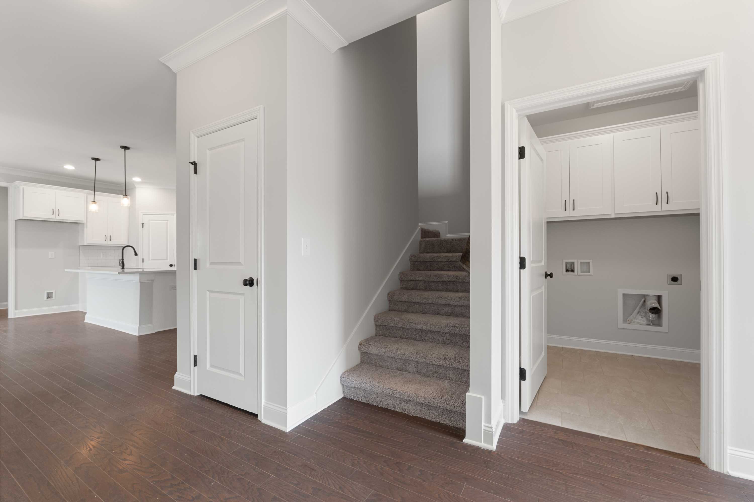 Main floor of The Copeland showcasing open kitchen with white cabinets, pendant lights, adjacent carpeted staircase, and laundry room