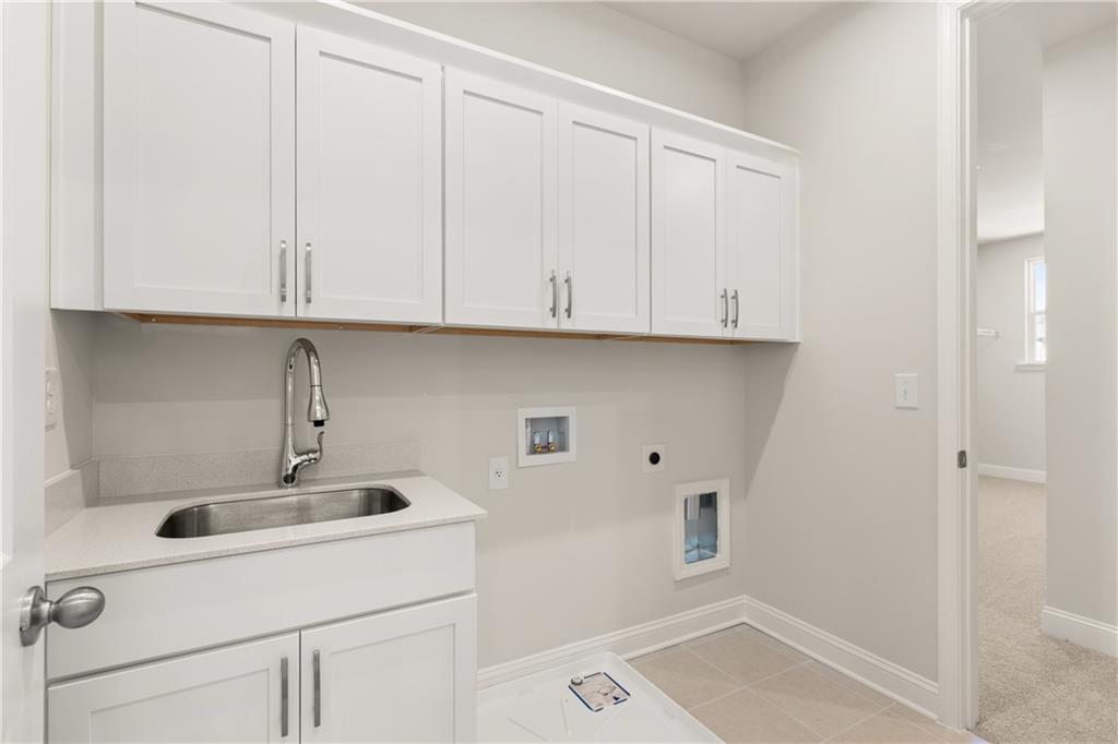 Modern laundry room with white shaker cabinets, deep stainless sink, pet door, and tiled floor in Davidson Homes The Danbury C, Buford, GA