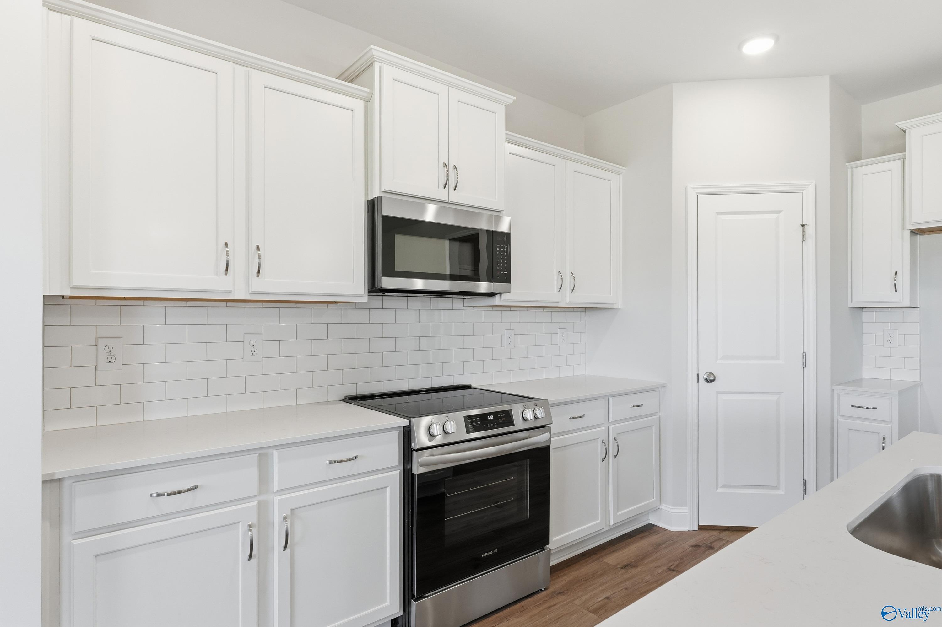 Modern white kitchen featuring stainless steel appliances, subway tile backsplash, and quartz counters in Davidson Homes The Everett, Harvest, AL