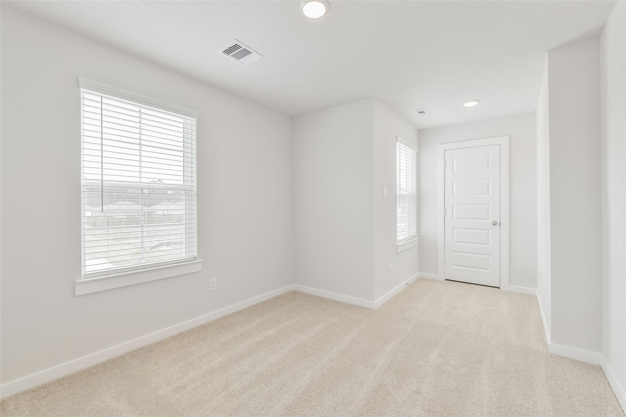 Bright secondary bedroom with beige carpet, white walls, and large window in The Brazos E by Davidson Homes, Cleveland, TX