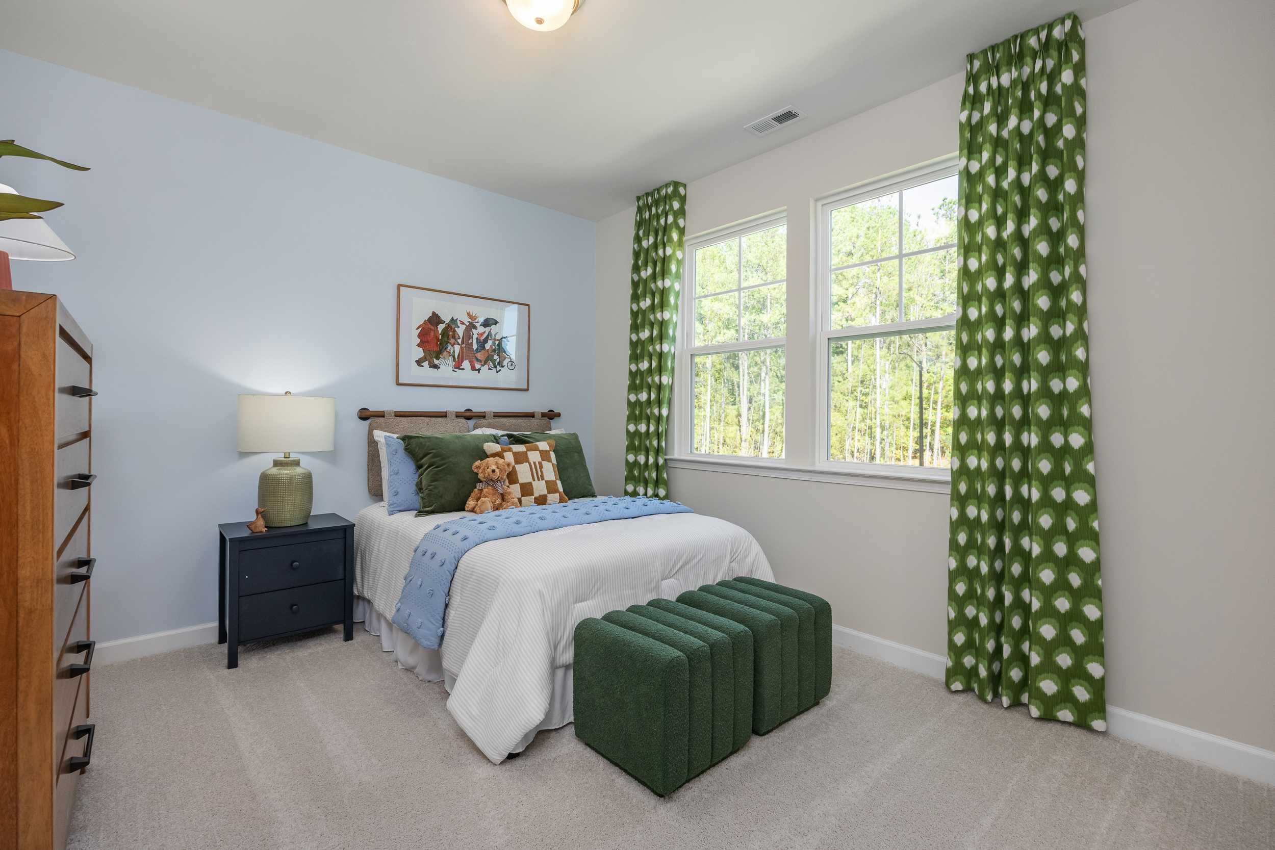 Cozy blue bedroom in The Hickory II E home featuring plush bed, green polka-dot curtains, fox artwork, and modern accents