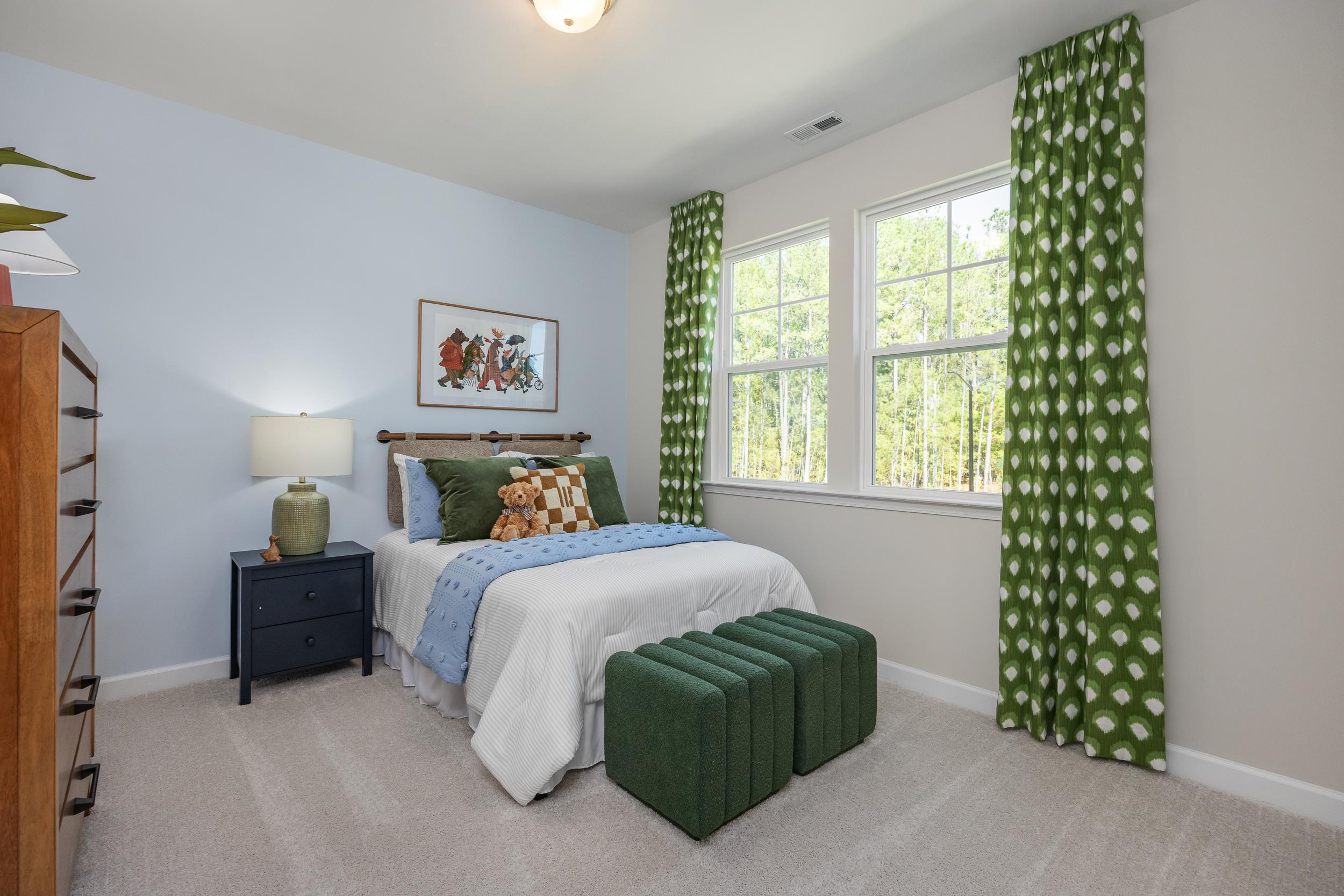 Cozy blue bedroom in The Hickory II E home featuring plush bed, green polka-dot curtains, fox artwork, and modern accents