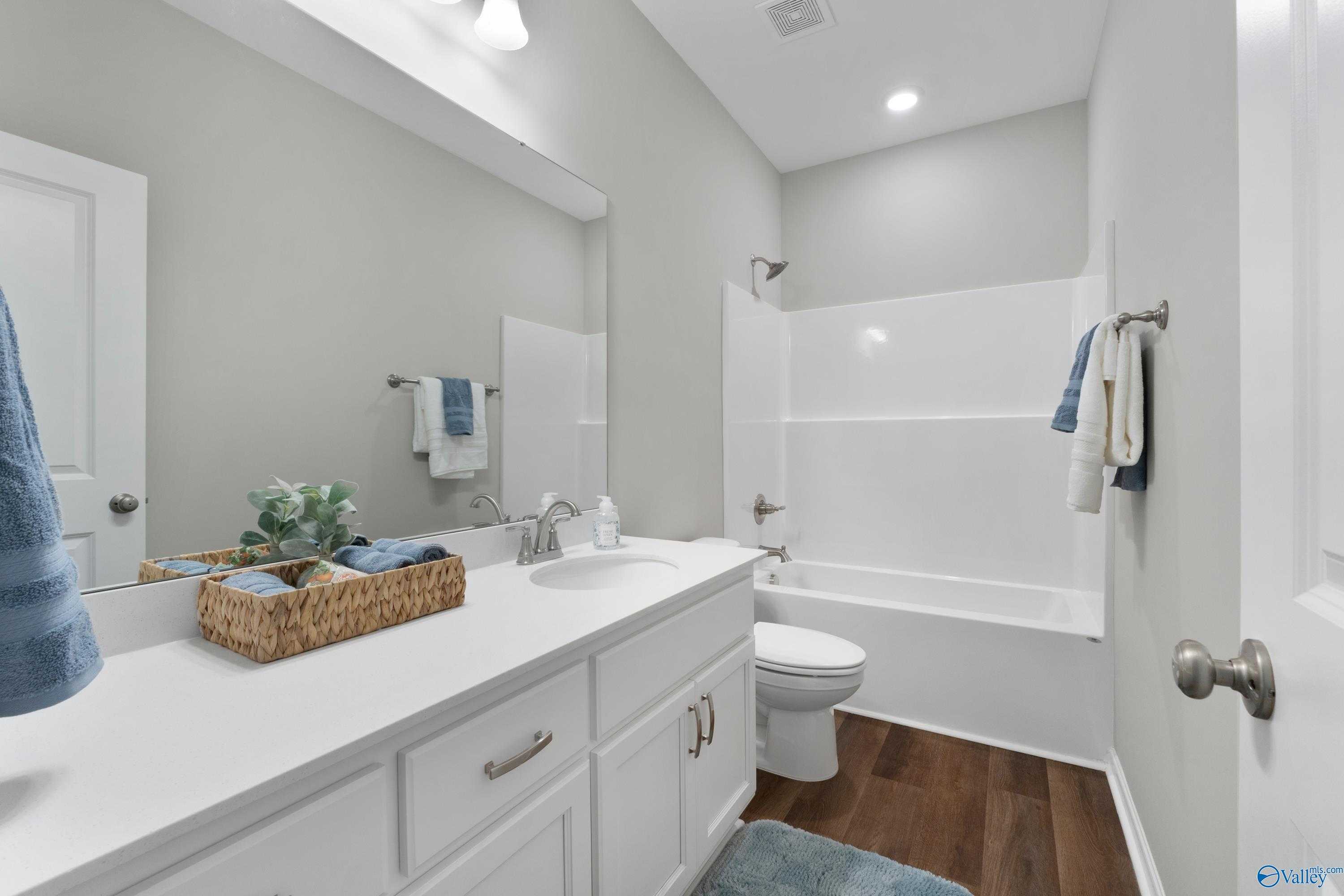 Bright bathroom with white vanity, tub-shower combo, toilet in Evermore Homes The Noble, Madison, Alabama