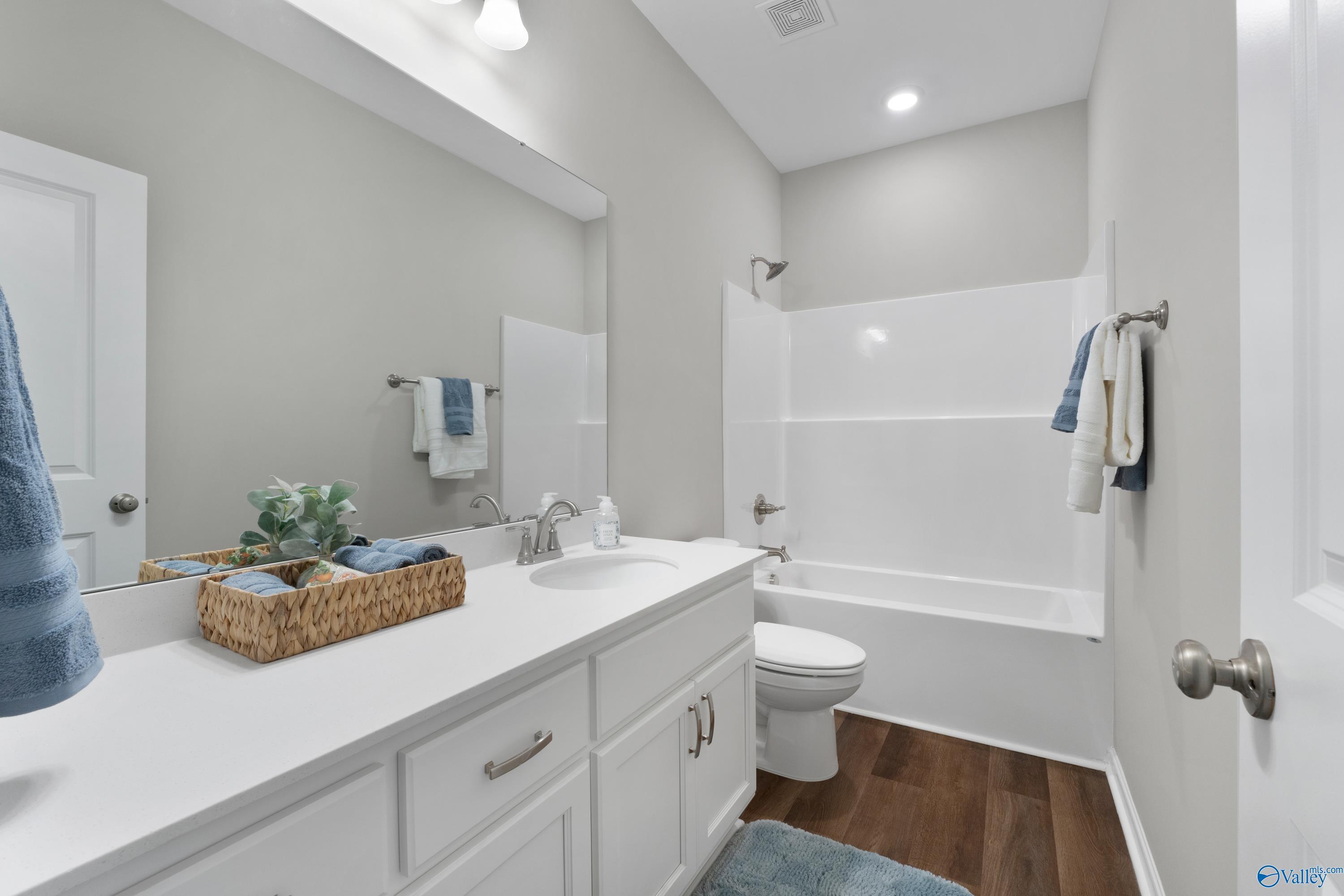 Bright modern bathroom with white vanity, tub-shower combo, toilet, and hardwood floors in Davidson Homes The Noble, Evergreen Mill, Madison, Alabama