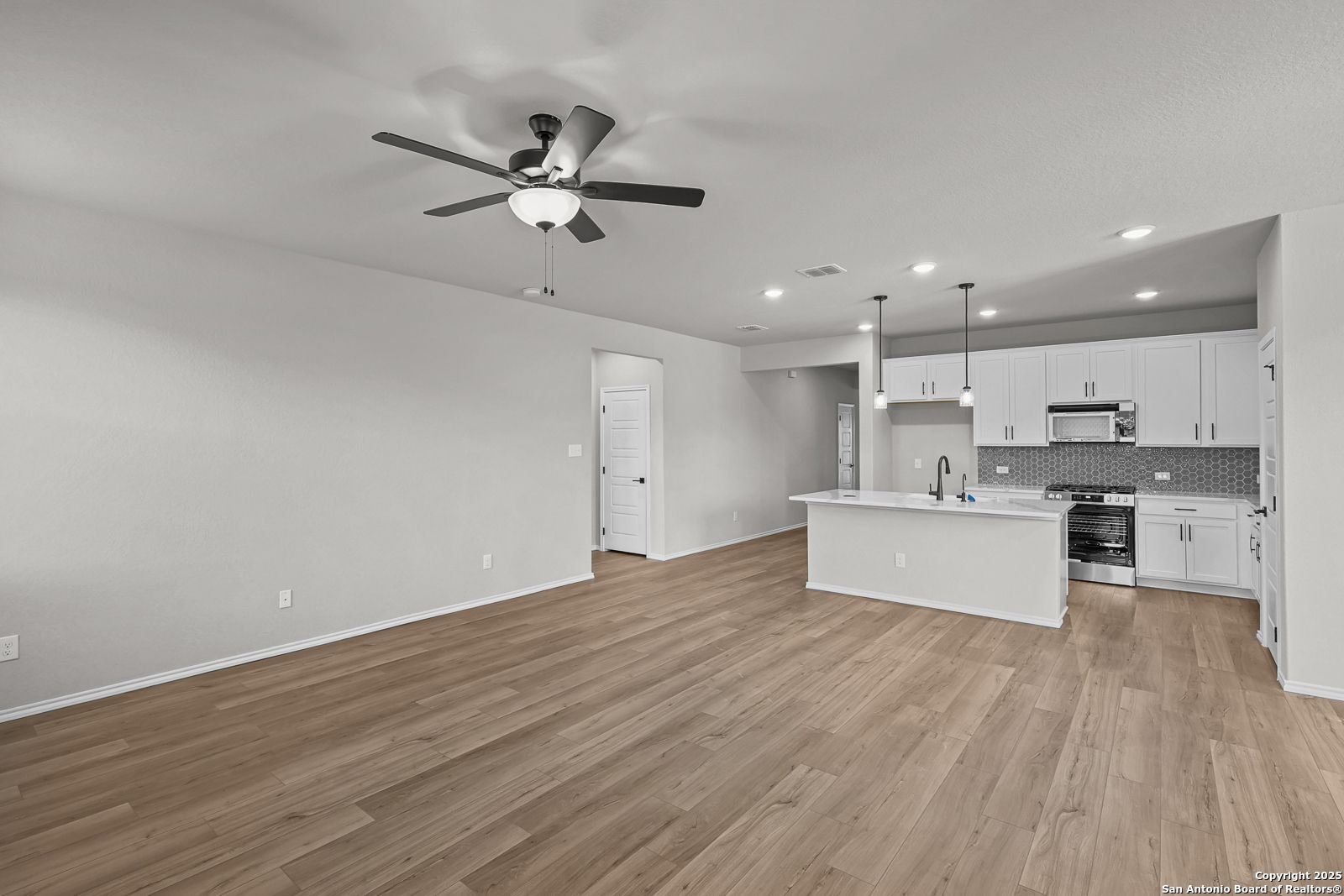 Open-concept living room and kitchen with white cabinets, island sink, wood laminate floors, and ceiling fan in Davidson Homes The Daphne K, San Antonio