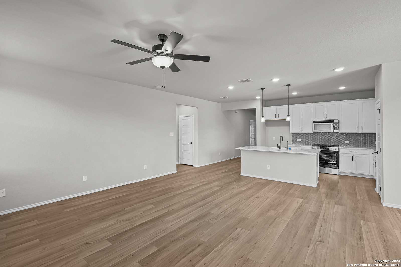 Modern open-concept kitchen with white cabinets, island, and hardwood floors in The Daphne K by Davidson Homes, San Antonio
