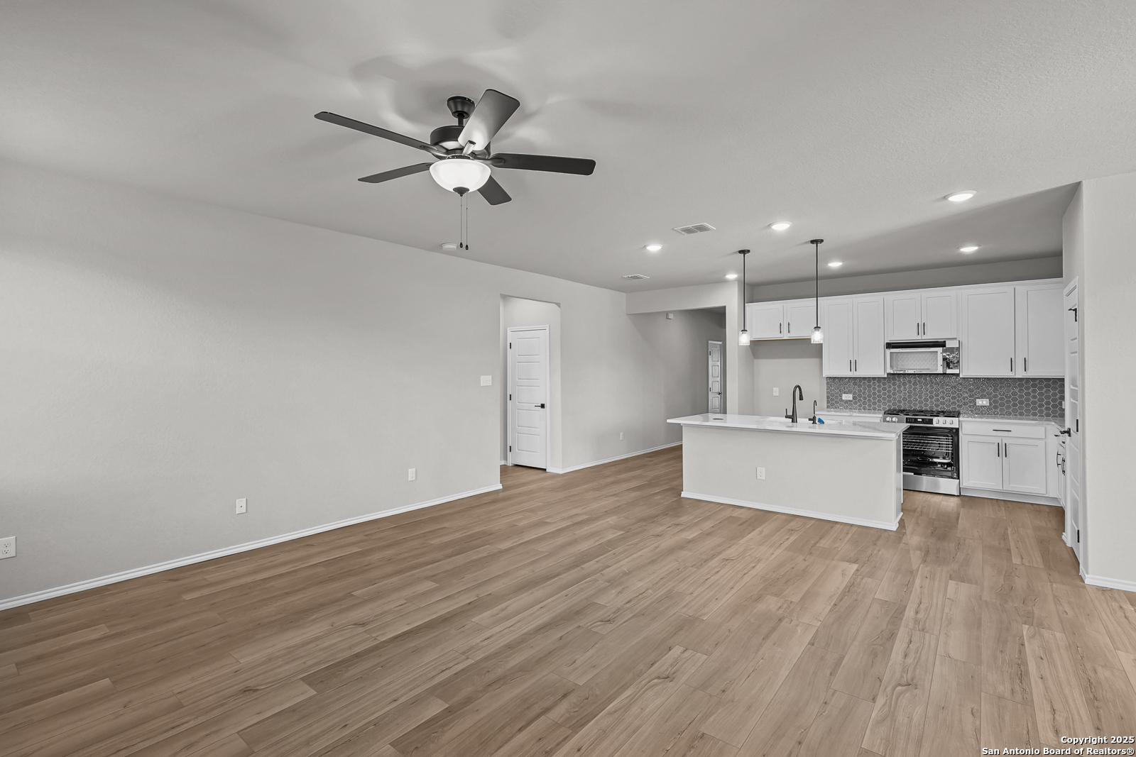 Open-concept living room and kitchen with white cabinets, island sink, wood laminate floors, and ceiling fan in Davidson Homes The Daphne K, San Antonio