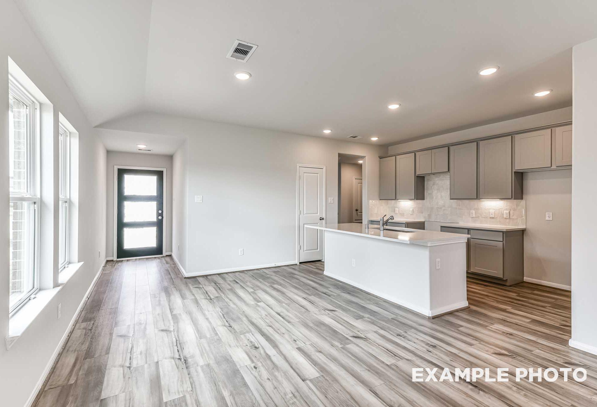 Open-concept kitchen and entry in The Costa A home by Davidson Homes, featuring white shaker cabinets, quartz island, hardwood floors, and large windows
