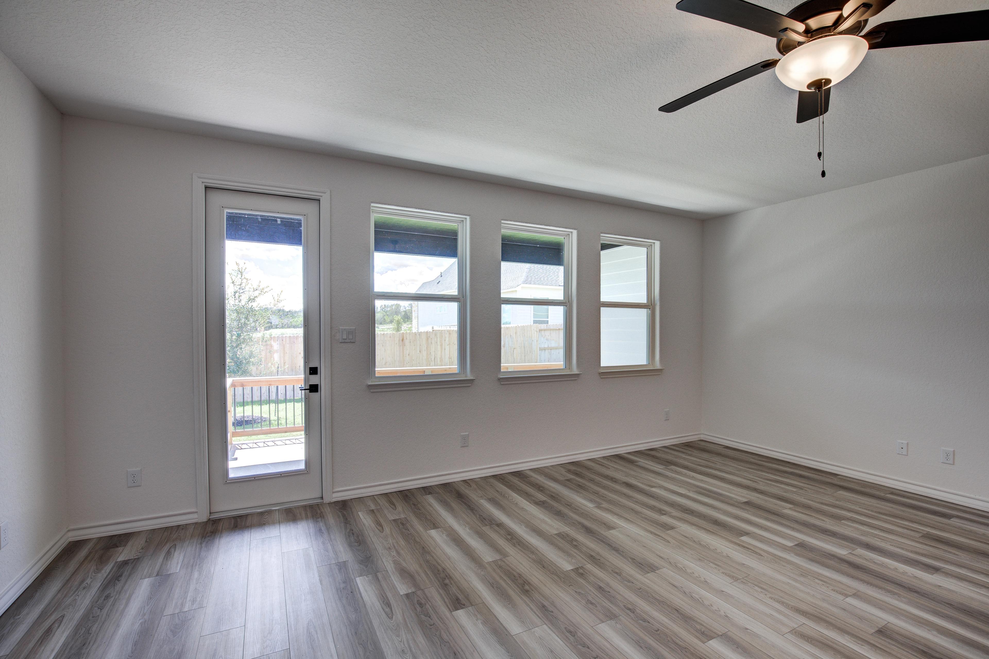 Spacious open living room in The Lanier floor plan featuring sliding glass door to backyard deck, large windows, and ceiling fan